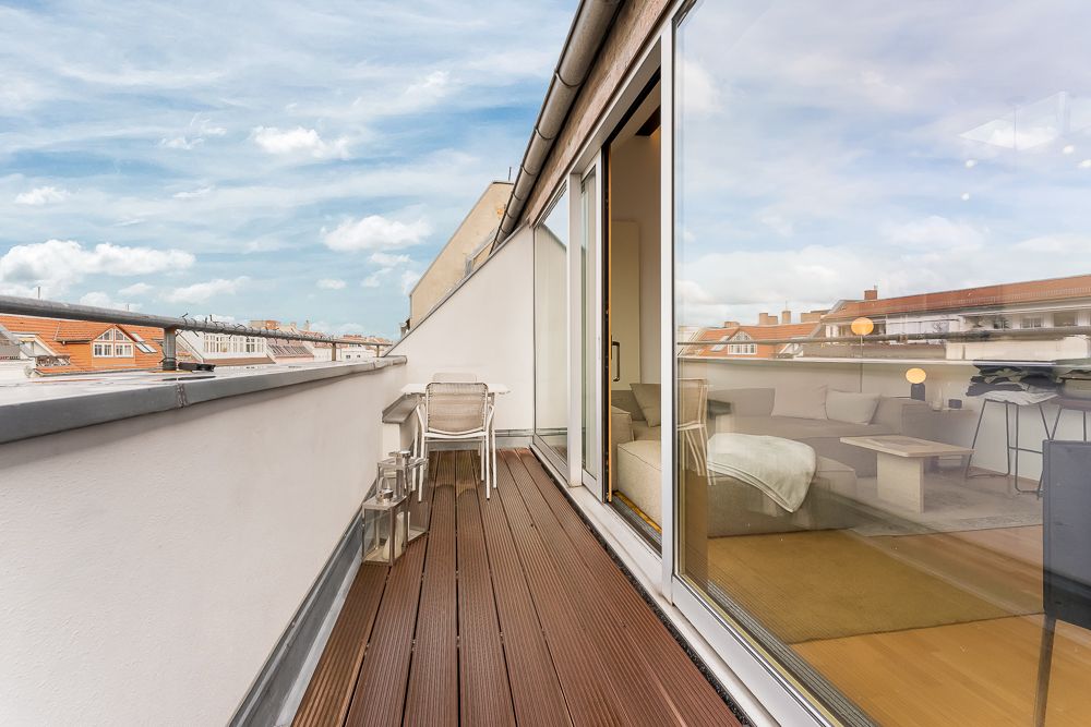 Schmaler Balkon mit Holzboden, Stuhl und Laternen, Blick ins Wohnzimmer durch große Glasschiebetür.