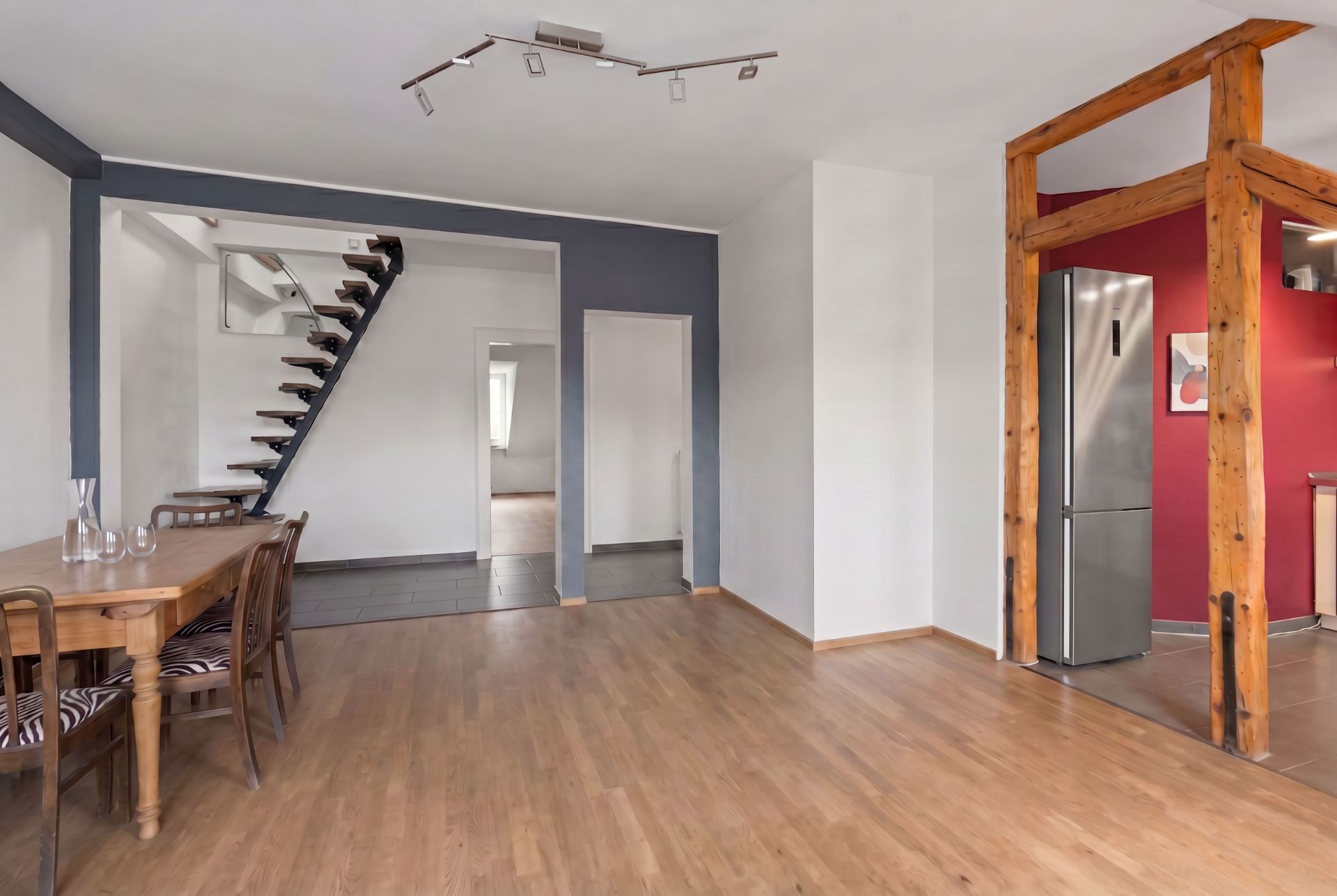Offener Wohnbereich mit Holzboden, Esstisch, moderner Treppe und sichtbaren Holzbalken.