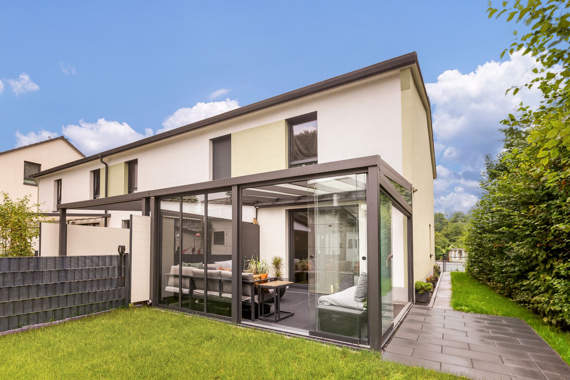 Modernes Wohnhaus mit verglastem Wintergarten und grünem Garten im Außenbereich.
