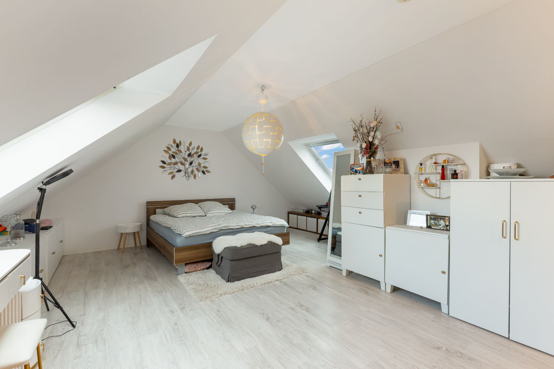 Helles Schlafzimmer mit Dachschrägen, Doppelbett, weißen Möbeln und Dachfenstern.