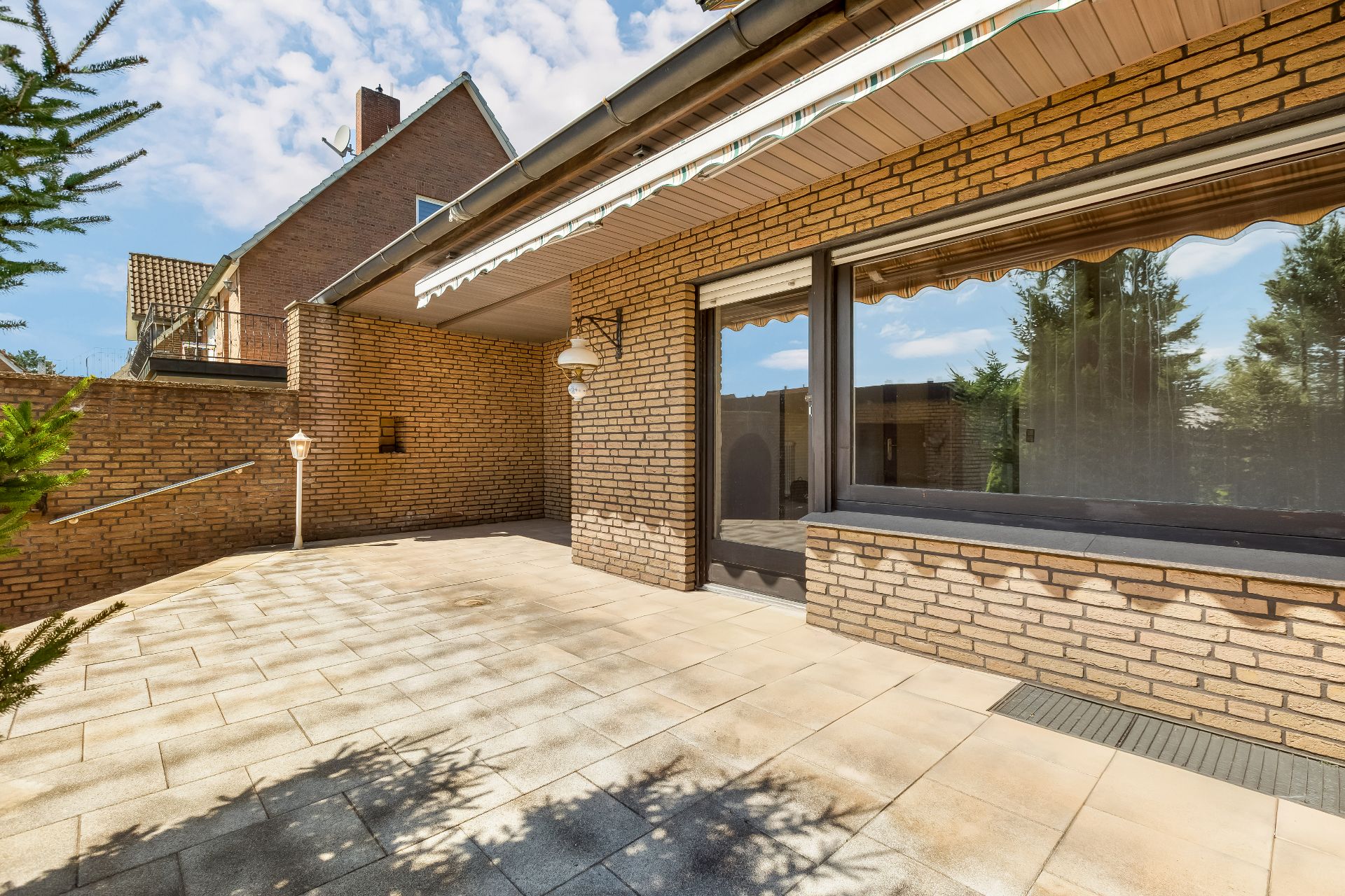 Große geflieste Terrasse mit Markise und Backsteinfassade.