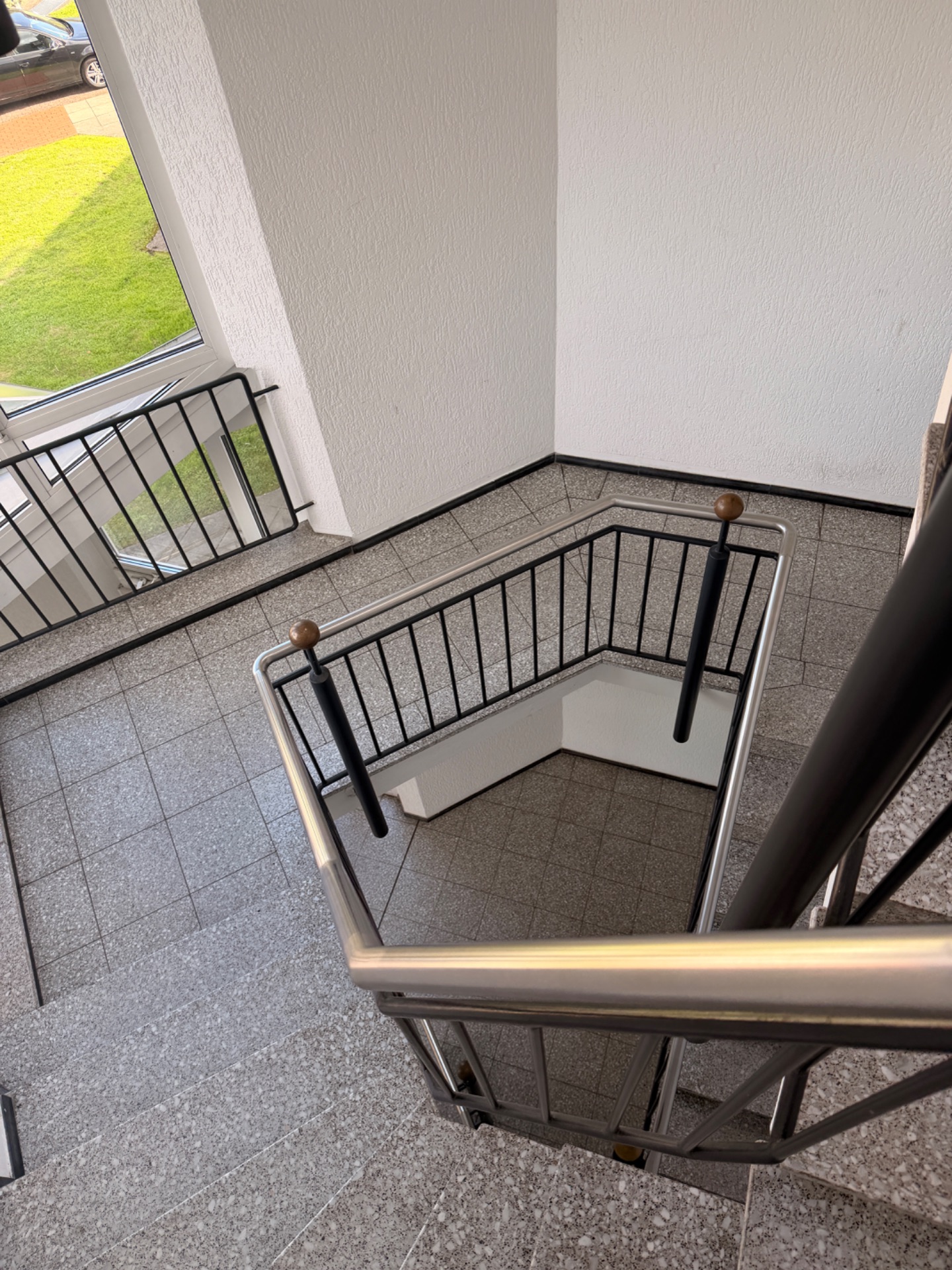 Ein Treppenhaus mit Metallgeländer und großen Fenstern, durch die grüner Rasen sichtbar ist.