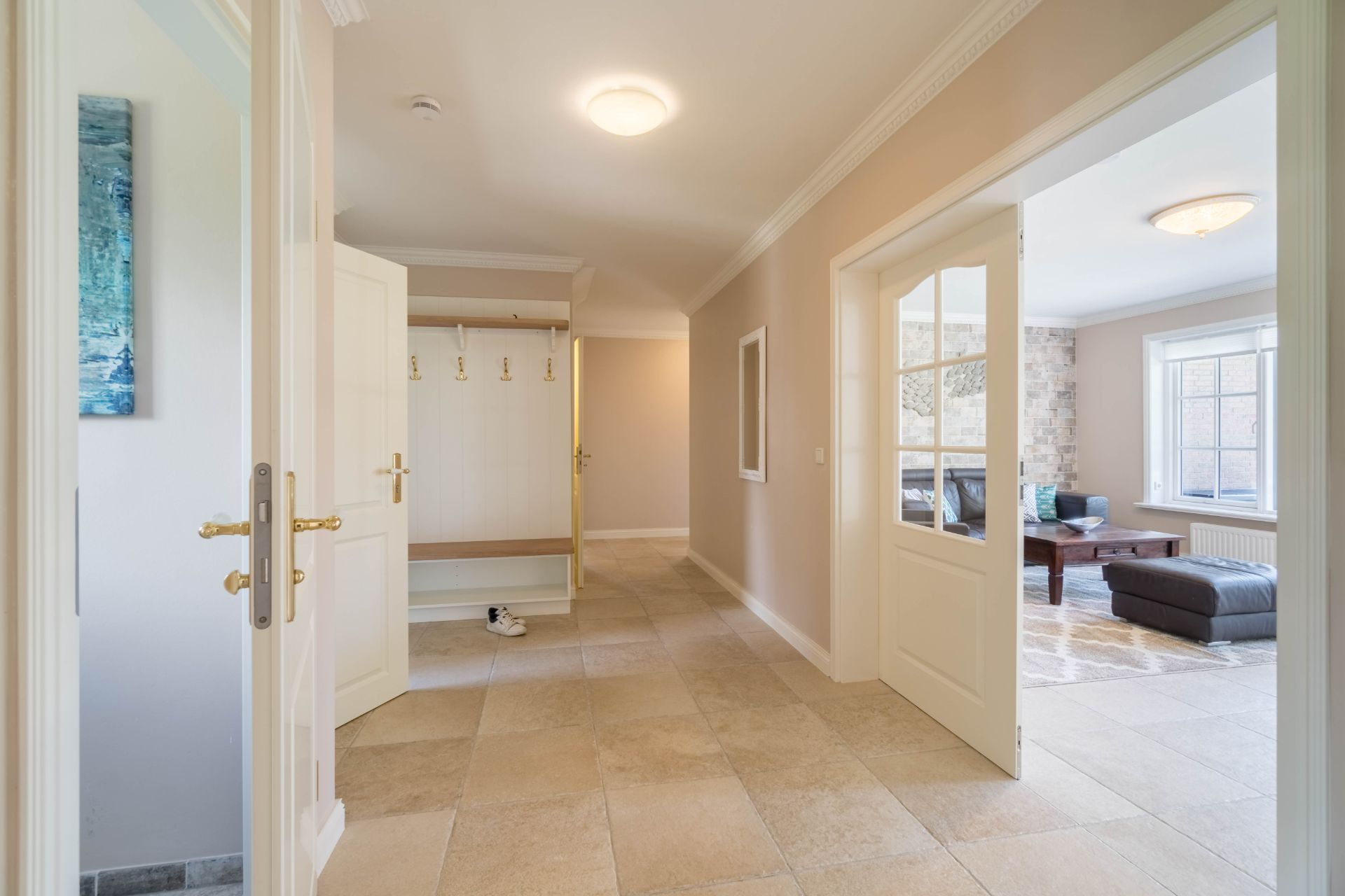 Heller Flur mit Garderobe, offenen Türen und Blick in ein Wohnzimmer mit Sofa.