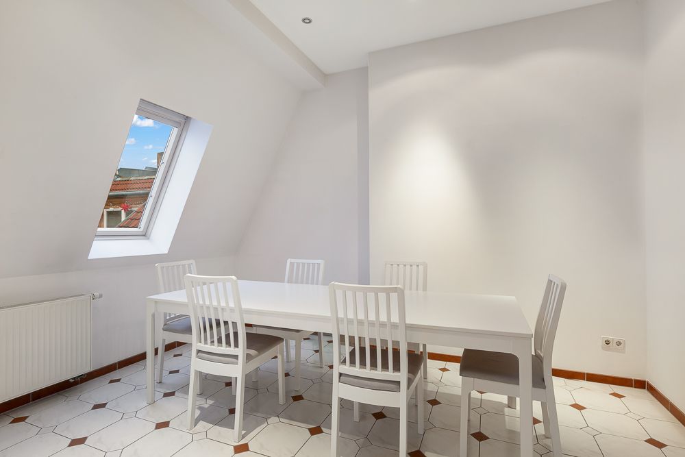 Heller Essbereich mit weißem Tisch, sechs Stühlen und schrägem Fenster.