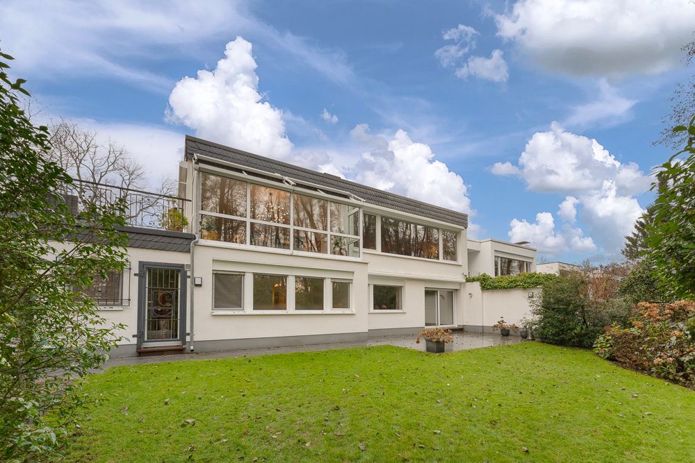 Moderne weiße Wohnhausfassade mit großen Fenstern und Garten bei Tageslicht.