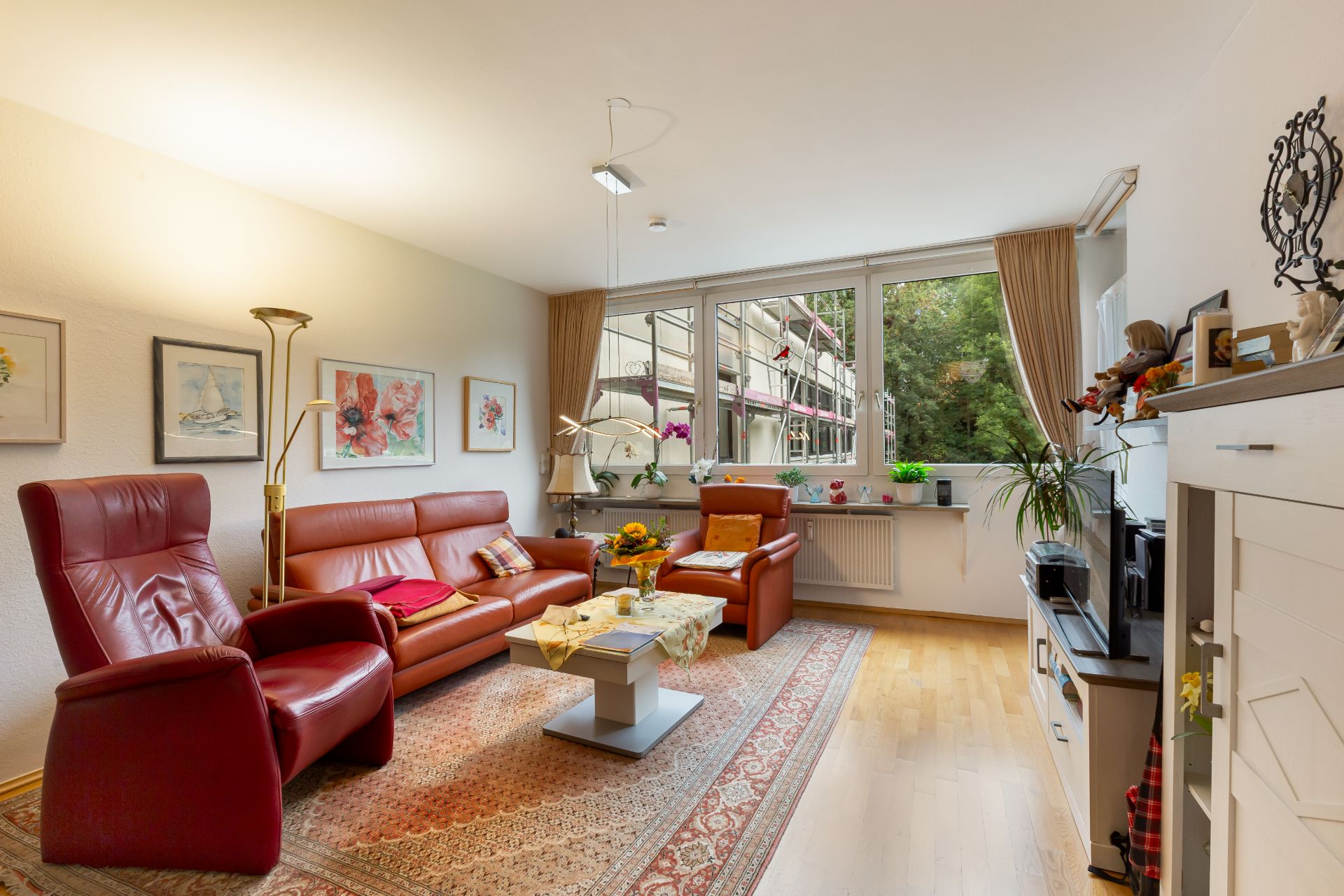 Helles Wohnzimmer mit roten Ledersesseln, Teppich, Couchtisch und großen Fenstern mit Blick nach draußen.