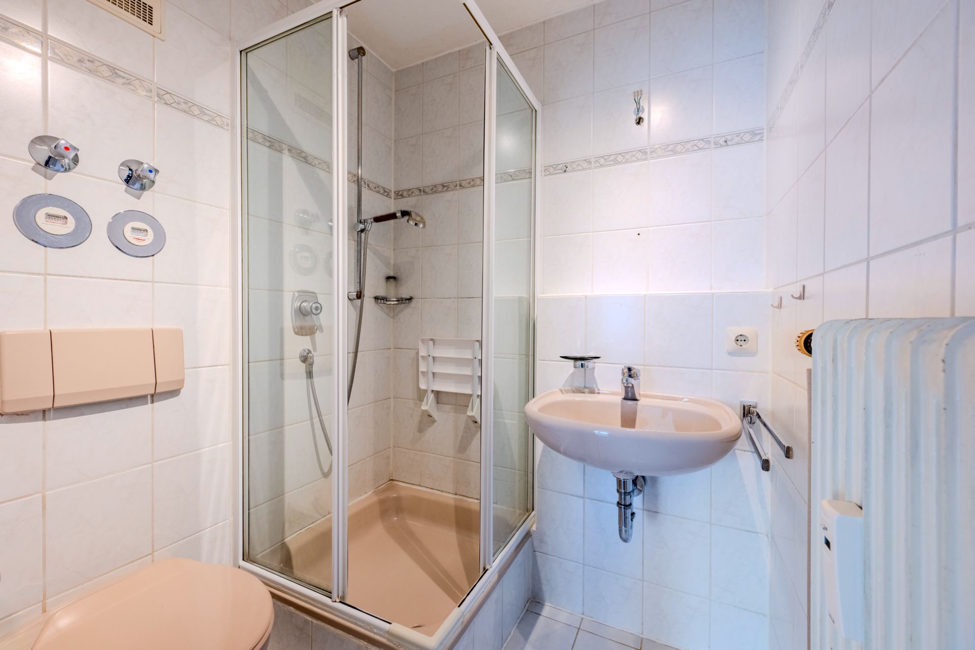 Kleines Badezimmer mit Dusche, WC, Waschbecken und Heizung, hell gefliest.