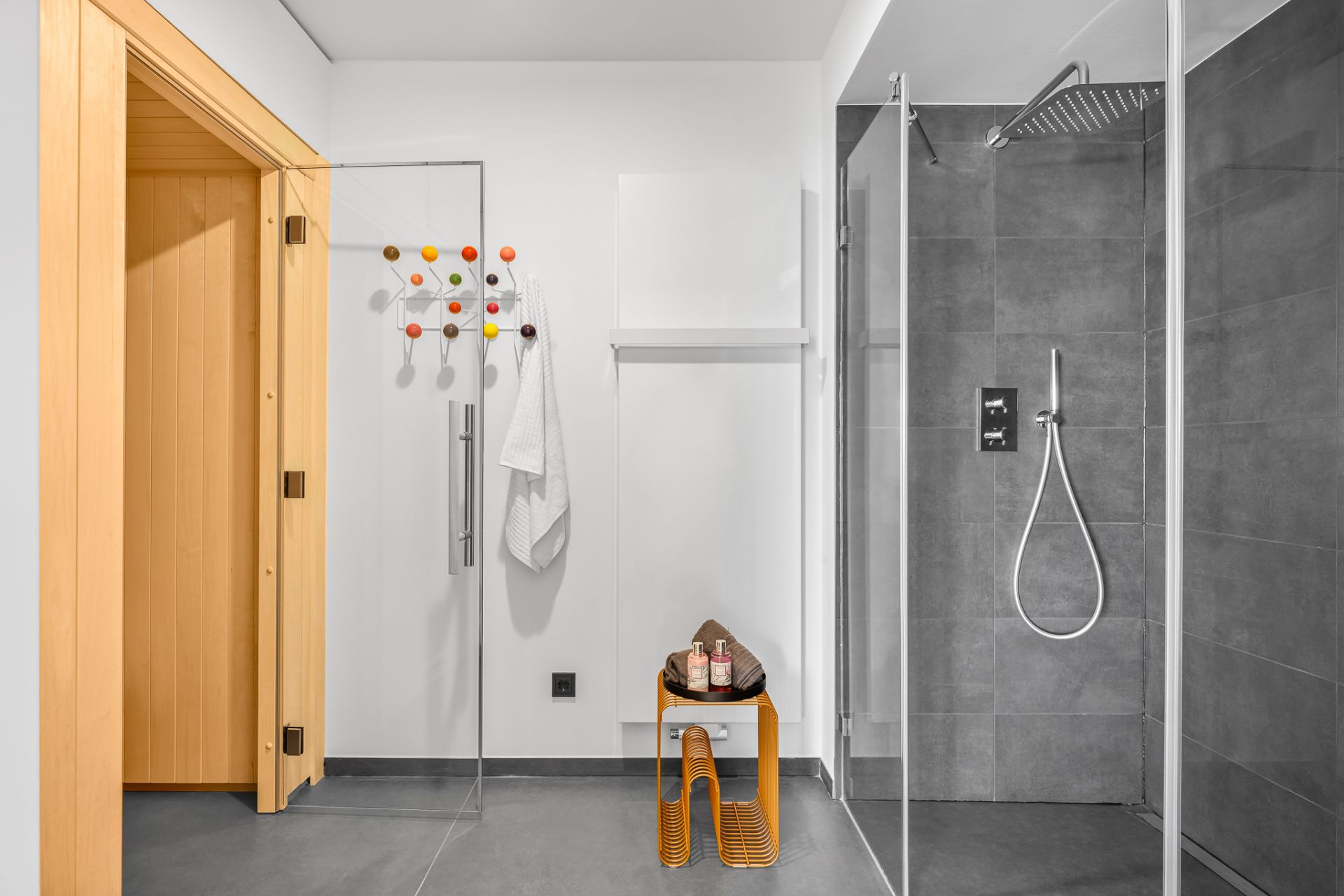 Modernes Badezimmer mit Dusche, Sauna, buntem Wandhaken und kleinem Tisch mit Handtüchern.