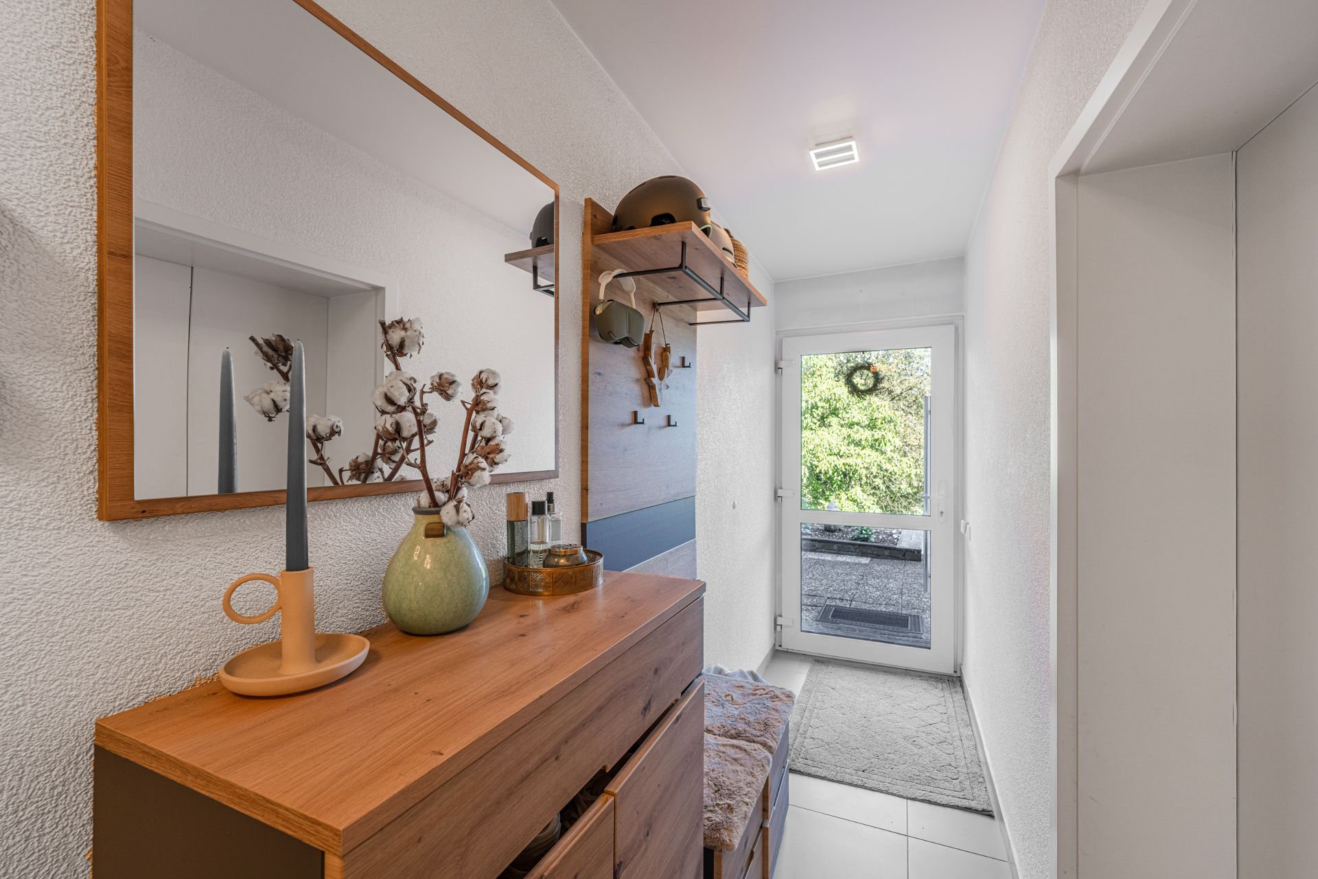 Heller Flur mit Holzmöbeln, Spiegel, Dekorationen und Glastür zum Garten.