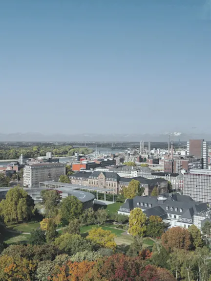 Blick auf eine Stadt mit Parks, Bäumen und mehreren Gebäuden bei klarem Himmel.