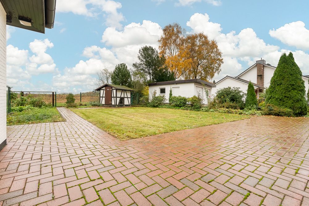 Gepflasterter Hof mit Rasenfläche, Gartenhaus und angrenzendem Wohnhaus.