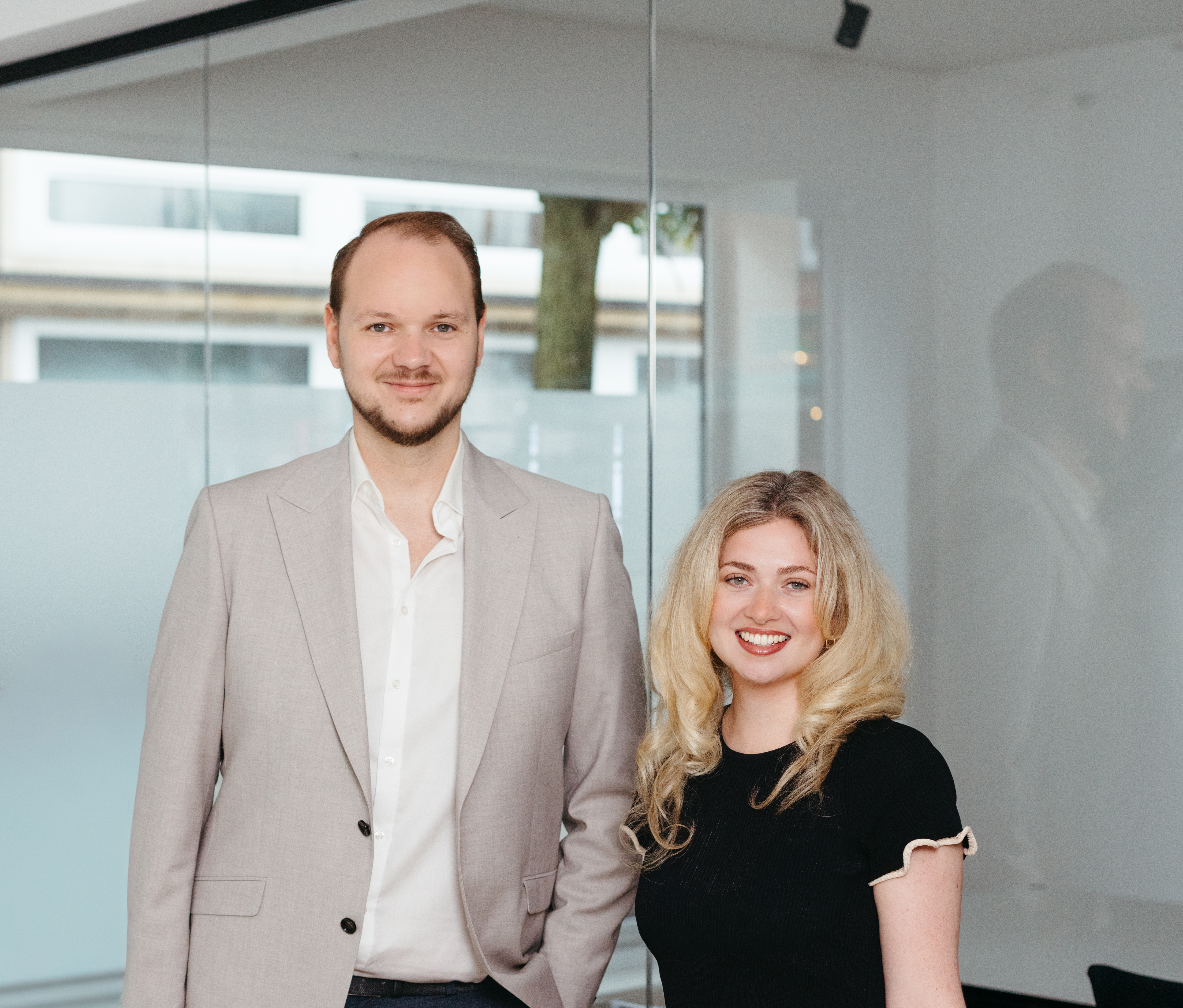 Ein Mann und eine Frau stehen nebeneinander in einem modernen, hellen Büro mit Glastüren.