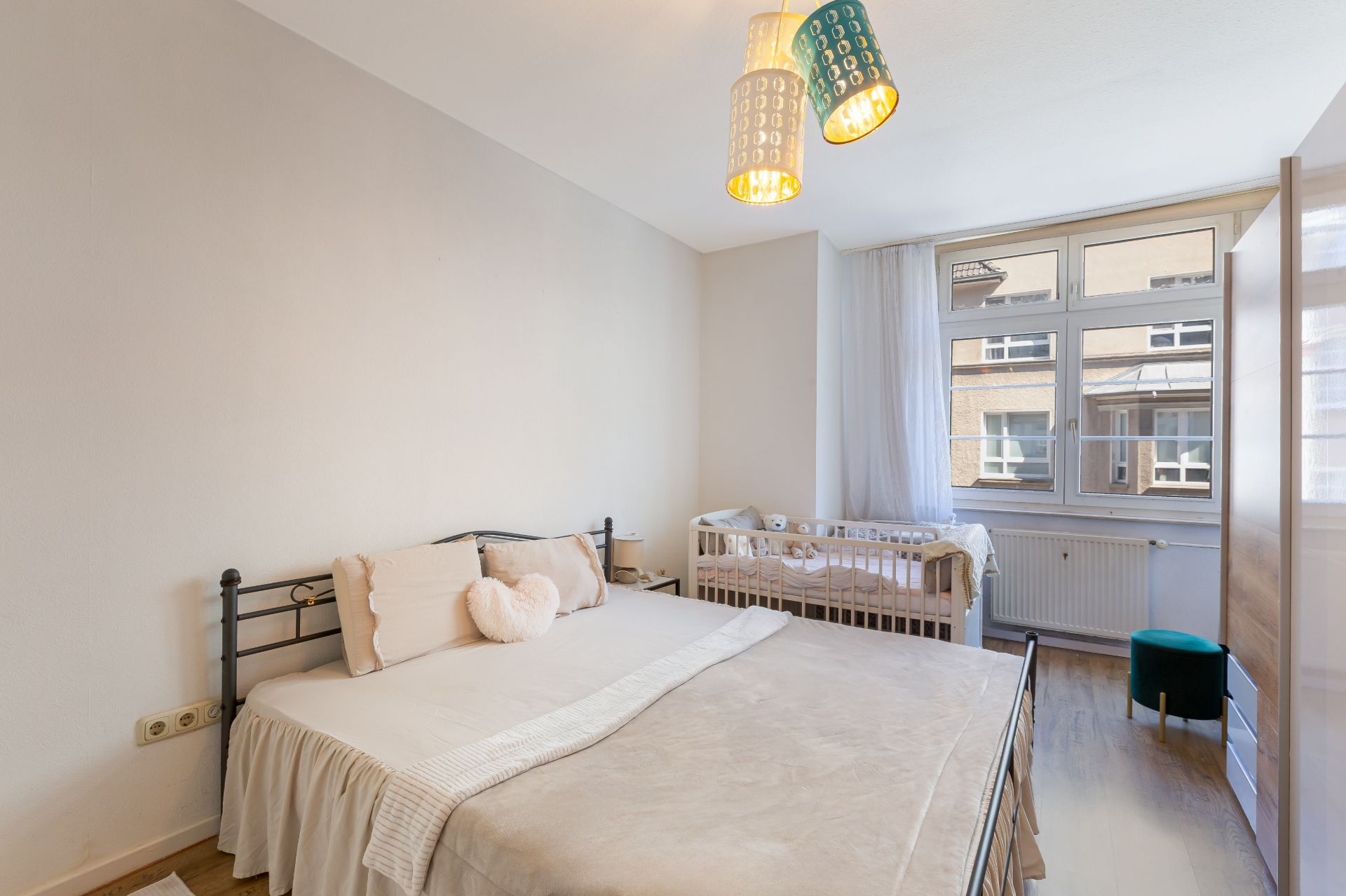 Helles Schlafzimmer mit Doppelbett, Babybett, großem Fenster und Kleiderschrank.