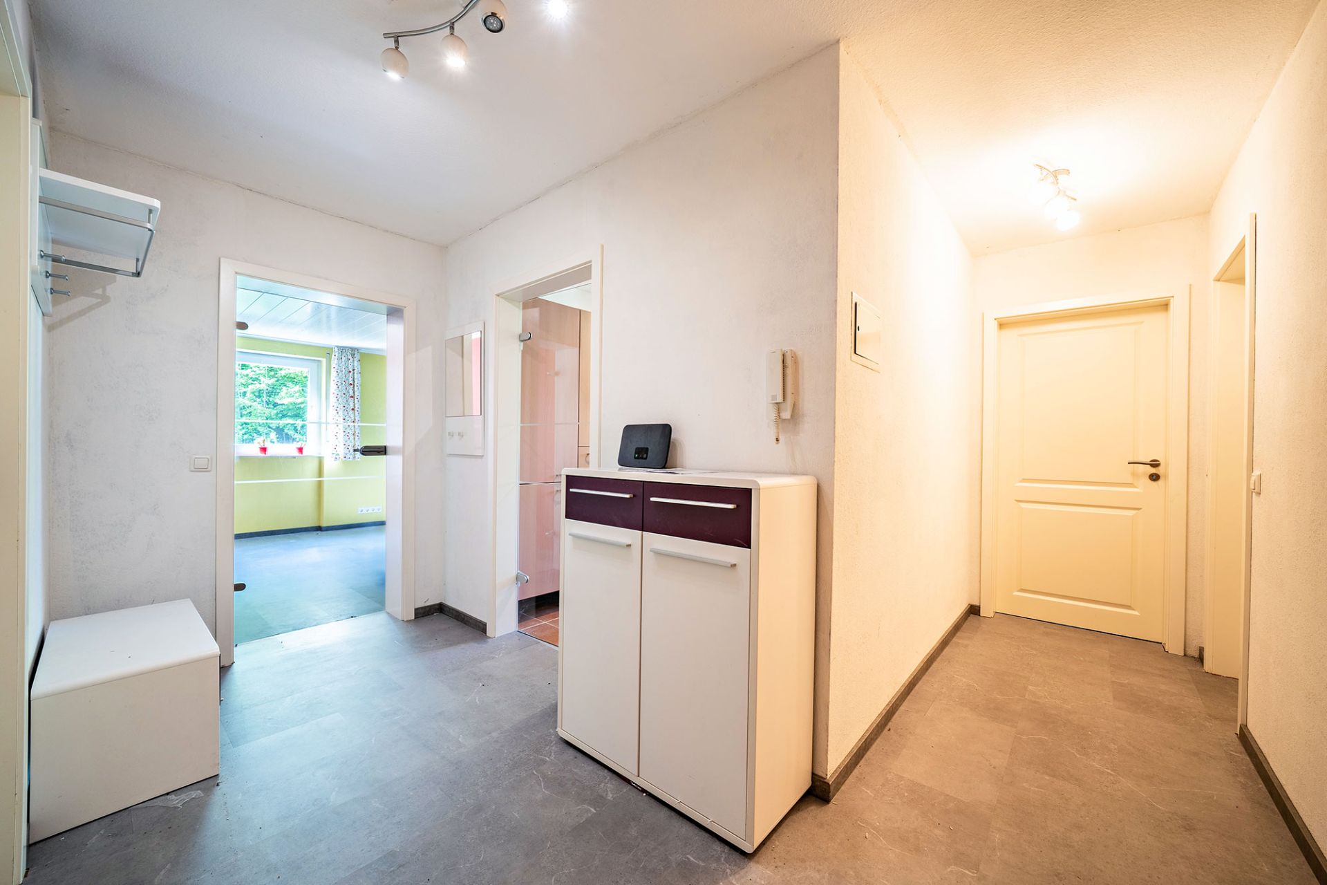 Heller Flur mit Kommode, weißen Türen und Blick in ein Zimmer mit grün gestrichener Wand.