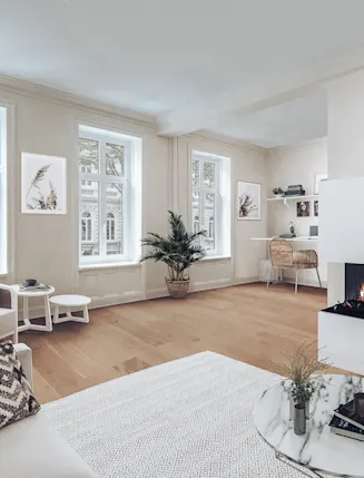 Helles Wohnzimmer mit Sofa, Sessel, Kamin, Schreibtisch und großen Fenstern.