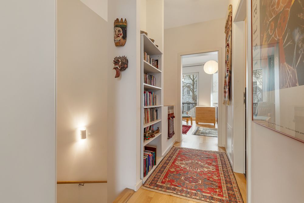Heller Flur mit Bücherregal, Wandmasken, rotem Teppich und Blick in ein Wohnzimmer.