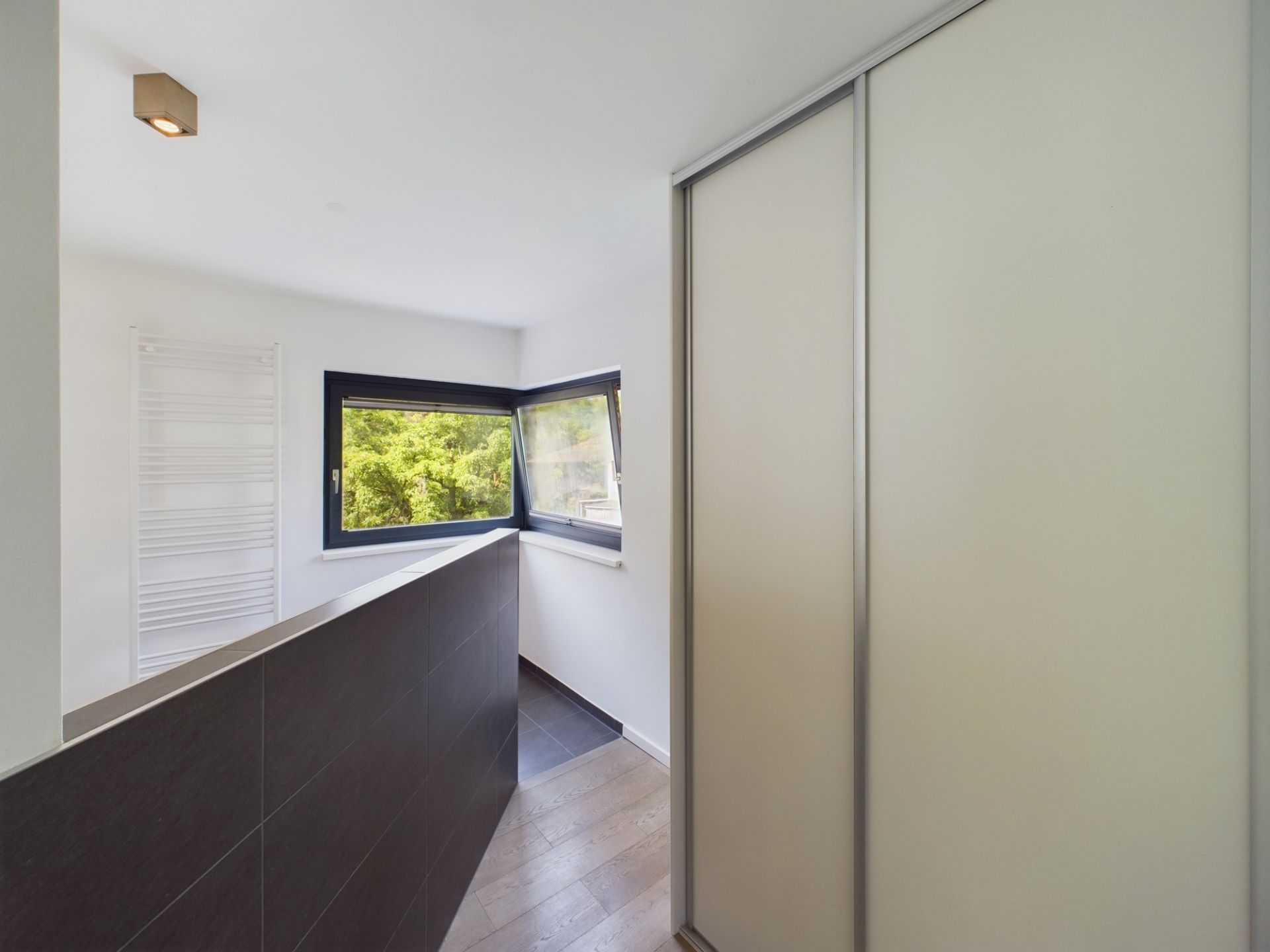 Heller Flur mit großem Fenster, Heizkörper und Schiebetürschrank.