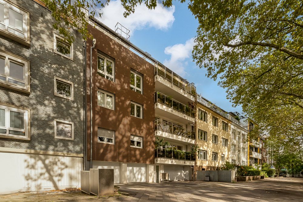 Mehrstöckiges Wohnhaus mit Balkonen und Bäumen davor bei Tageslicht.