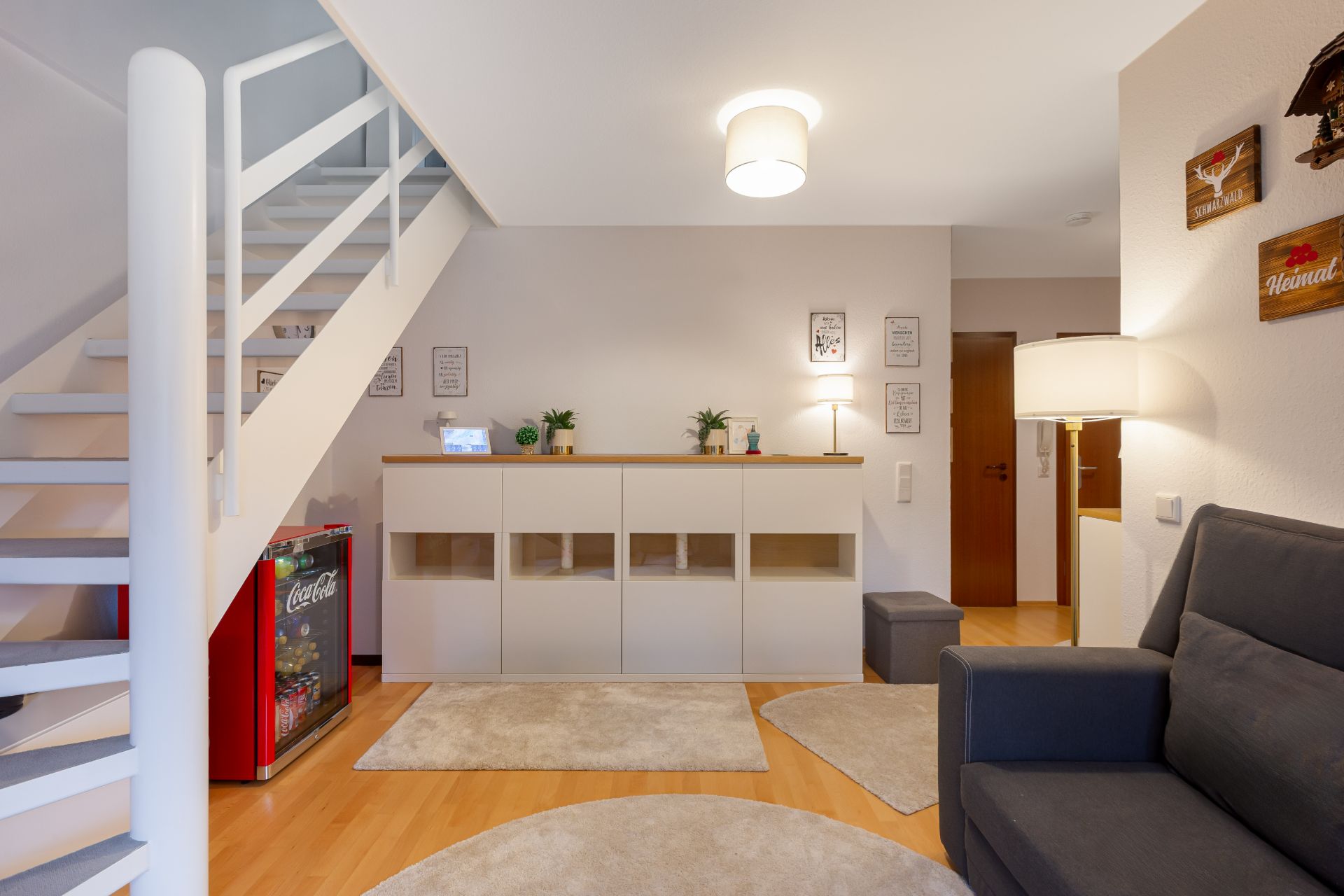 Wohnzimmer mit Sofa, Teppichen, Sideboard, Lampen und Treppe nach oben.