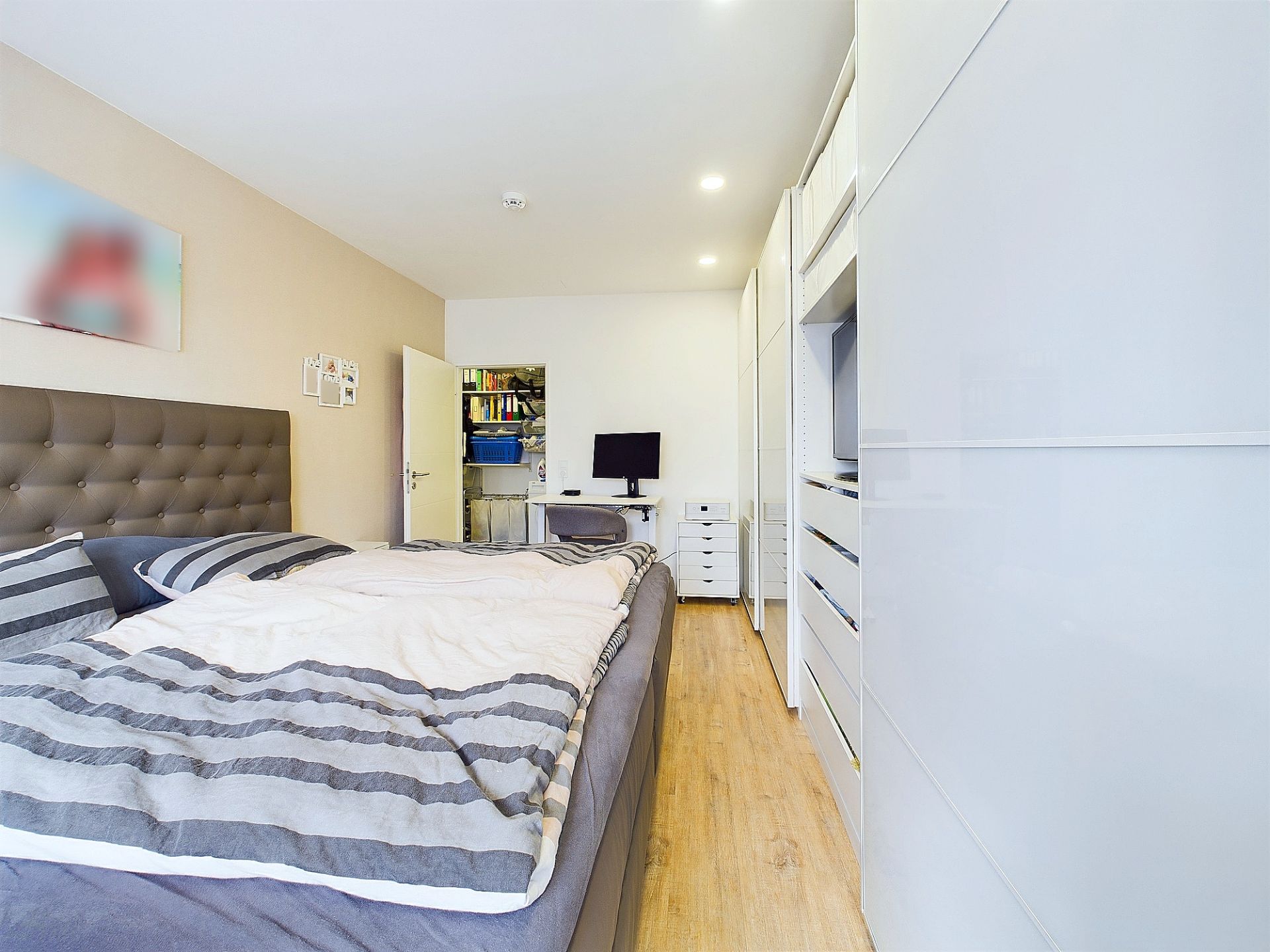 Modernes Schlafzimmer mit Doppelbett, Schreibtisch, weißem Kleiderschrank und Holzfußboden.