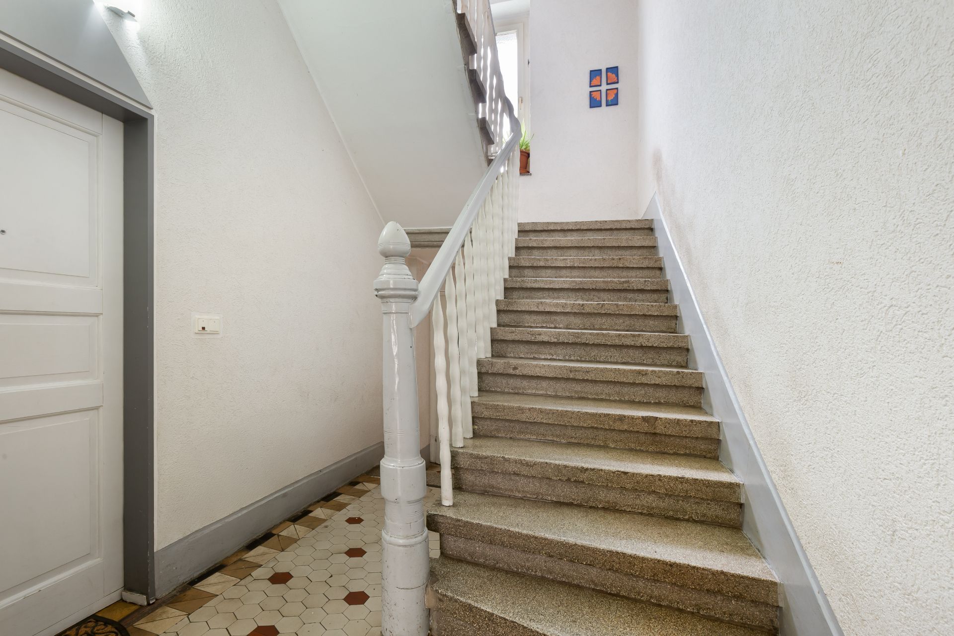 Helles Treppenhaus mit gefliester Etage und weißem Geländer in einem Wohnhaus.