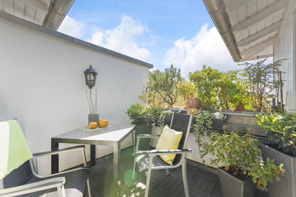 Kleine Terrasse mit zwei Stühlen, Tisch und vielen Pflanzen unter blauem Himmel.