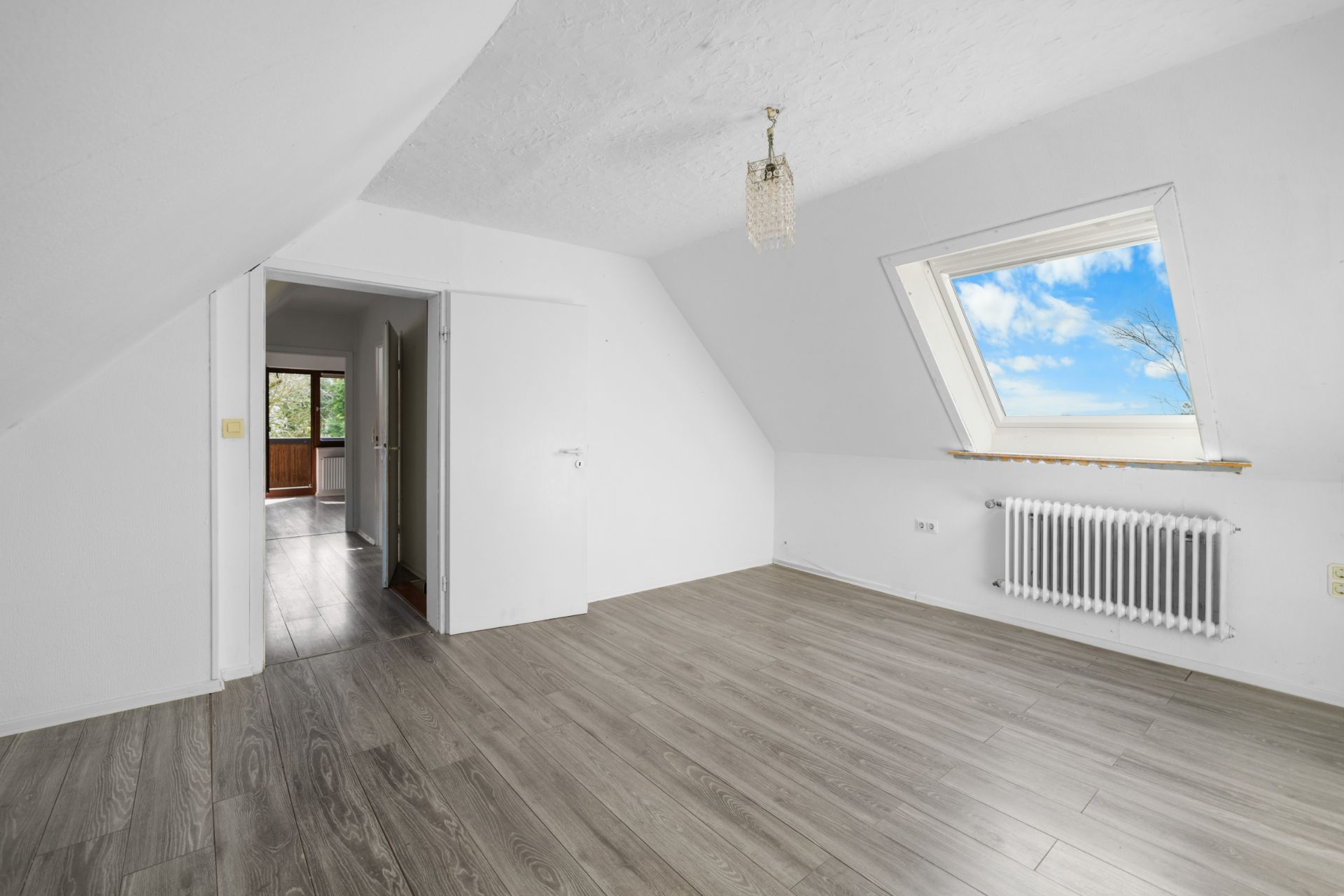 Helles Zimmer mit Dachschräge, Holzfußboden, Fenster und Heizkörper.