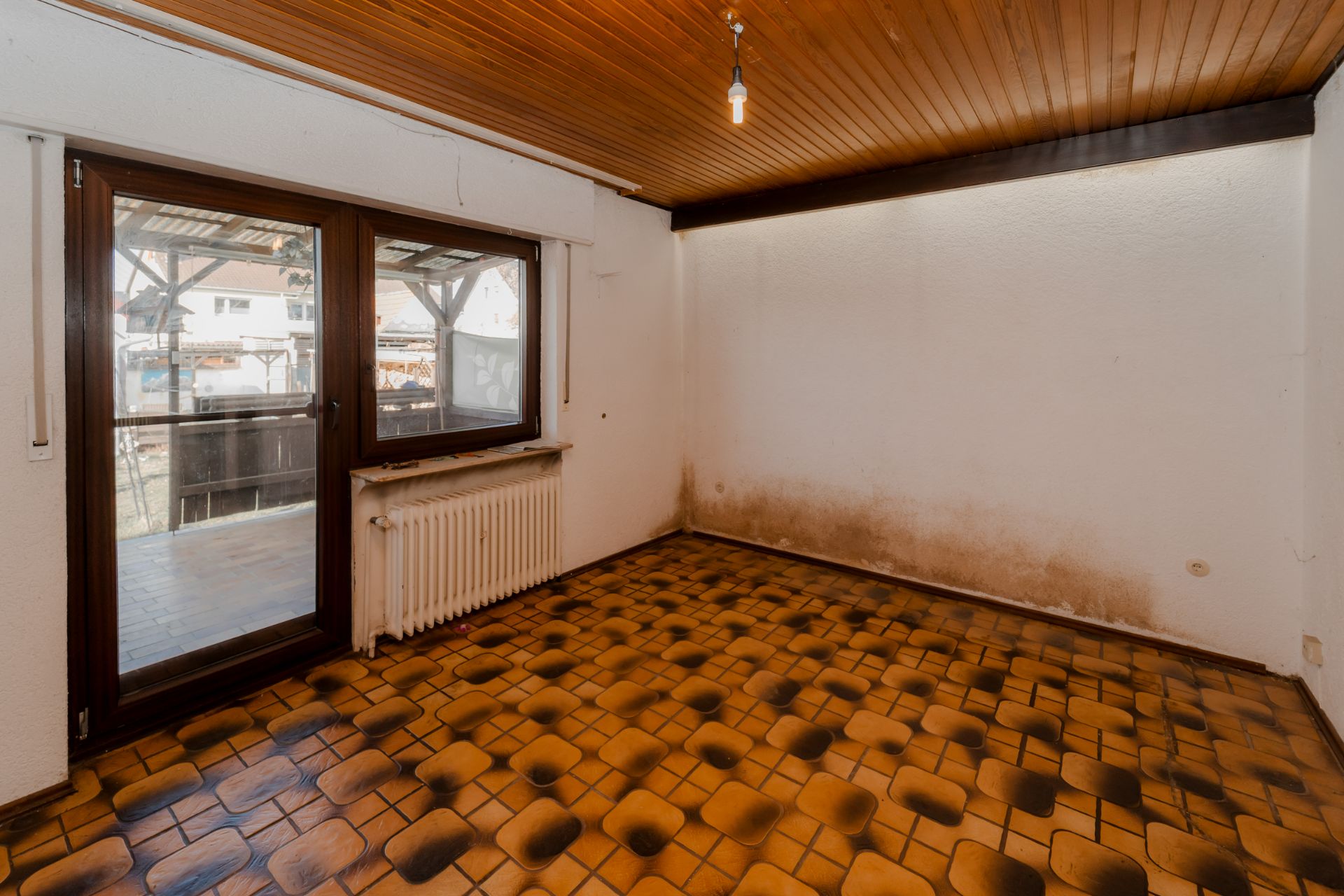 Leerer Raum mit braun gemustertem Boden, Holzbalkendecke und sichtbarer Fensterfront.