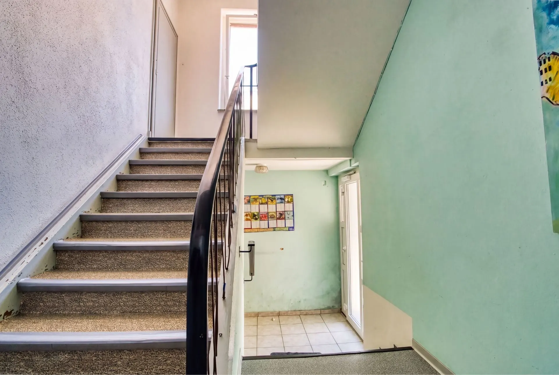 Treppenhaus mit Handlauf, grün gestrichene Wand und Briefkasten an der Wand.