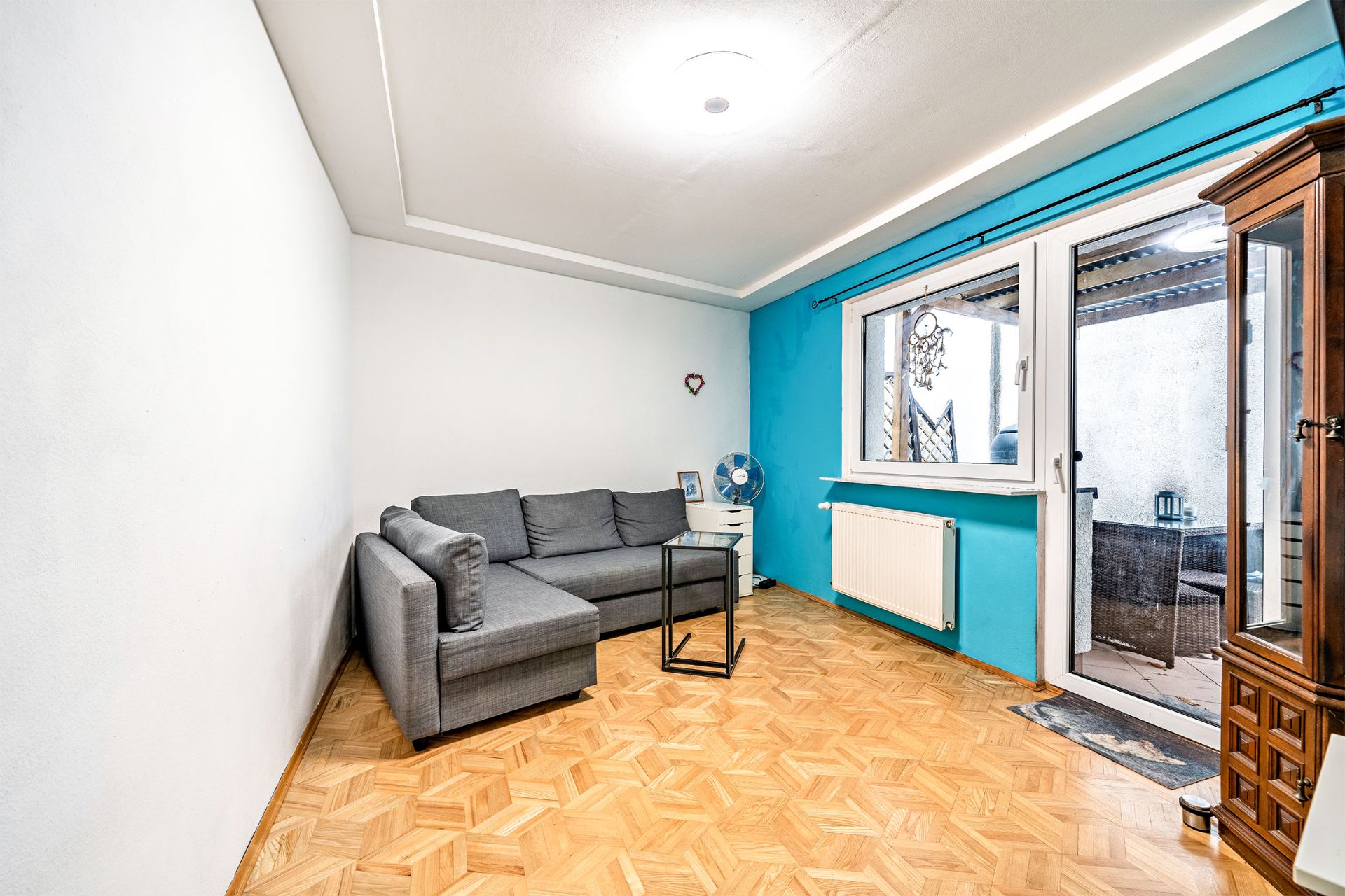 Wohnzimmer mit grauem Ecksofa, Glastisch, Parkettboden und Zugang zur Terrasse.