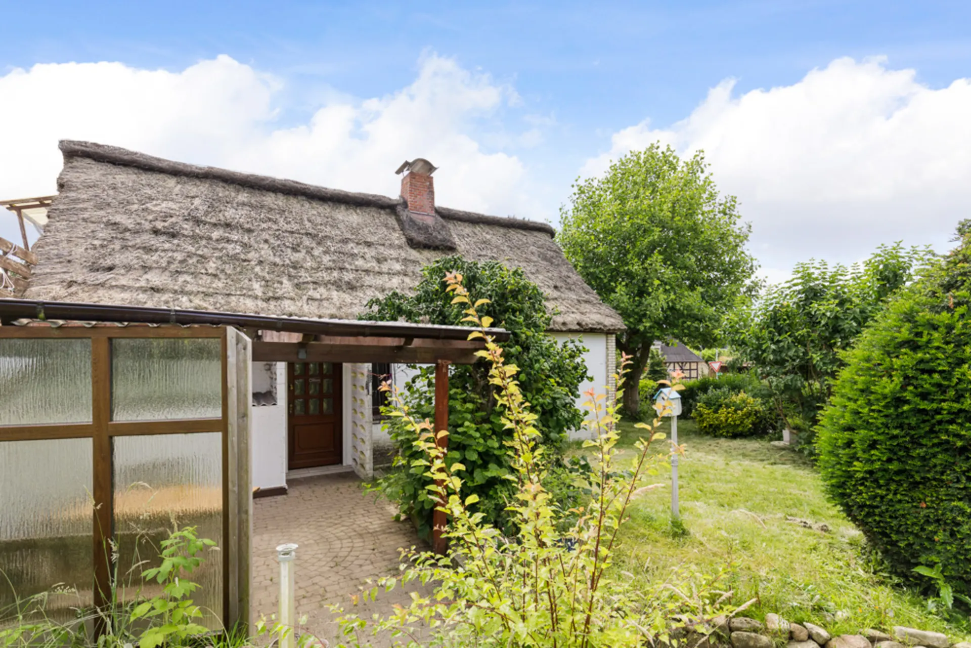 Ein weißes Haus mit Reetdach und Garten, umgeben von Bäumen und Sträuchern.