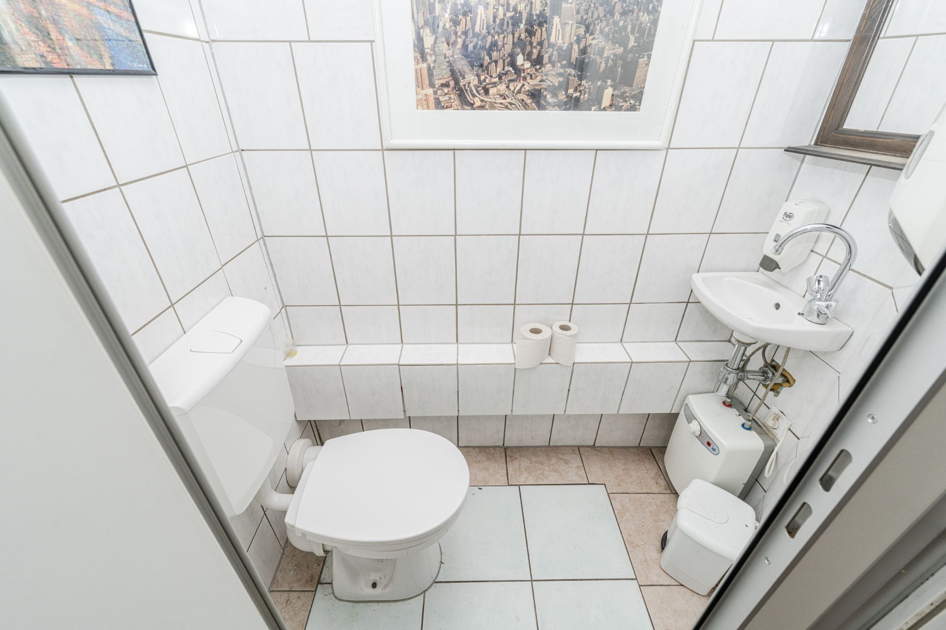 Kleines Bad mit Toilette, Waschbecken, Spiegel und zwei Toilettenpapierrollen.
