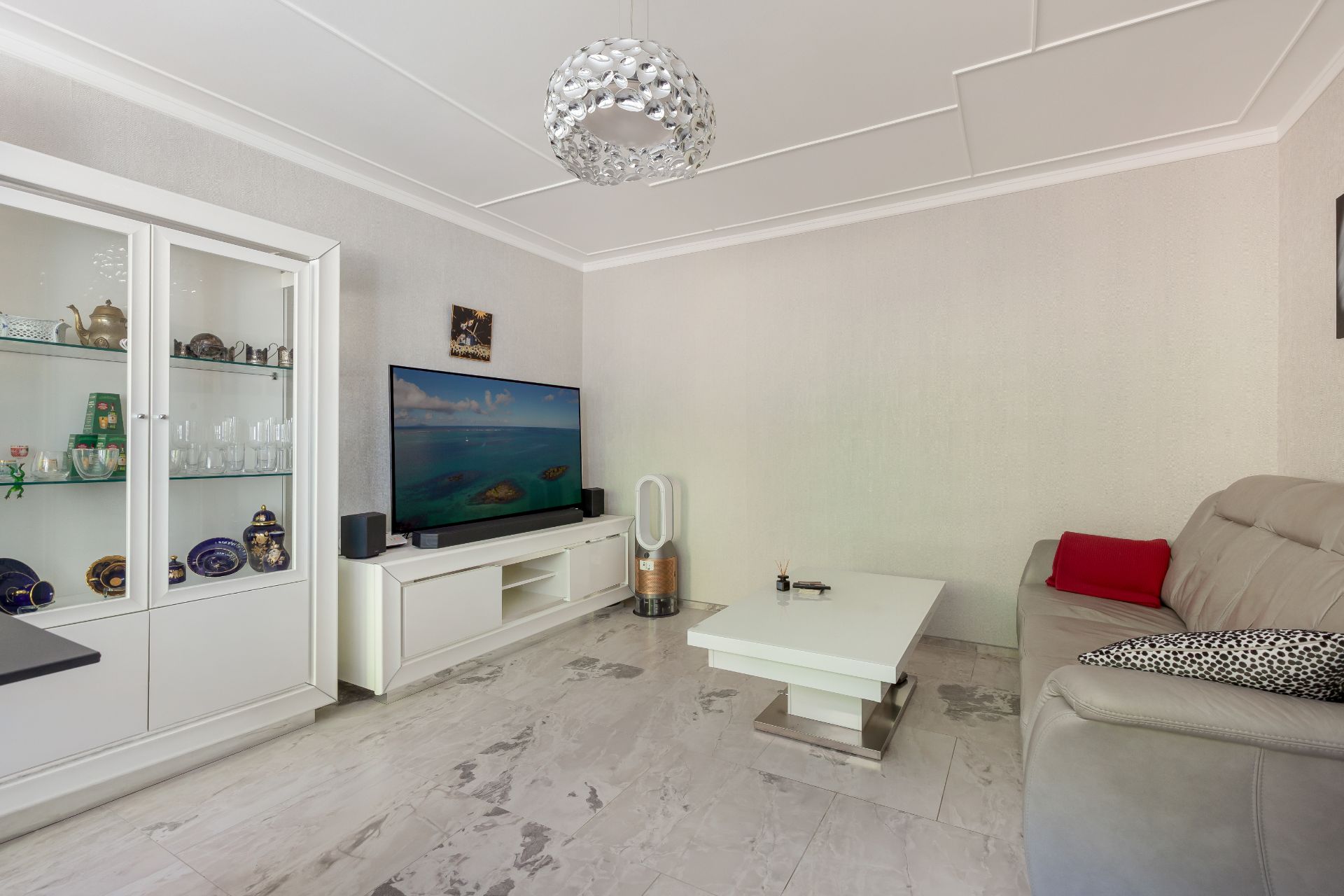 Modernes Wohnzimmer mit Sofa, Couchtisch, TV, Vitrine und heller Fliese.