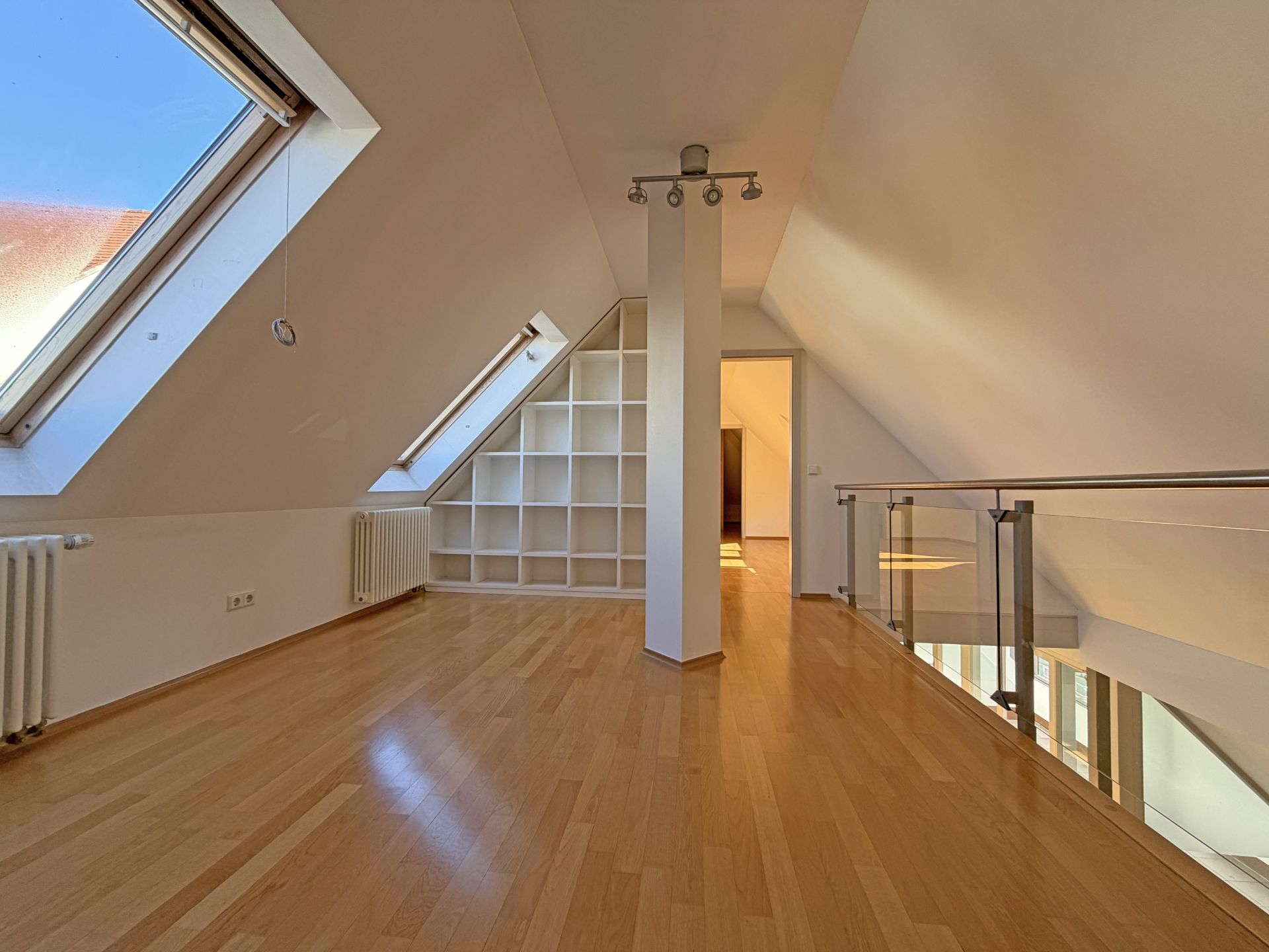 Heller Dachgeschossraum mit Holzboden, schrägen Fenstern und Regalwand.
