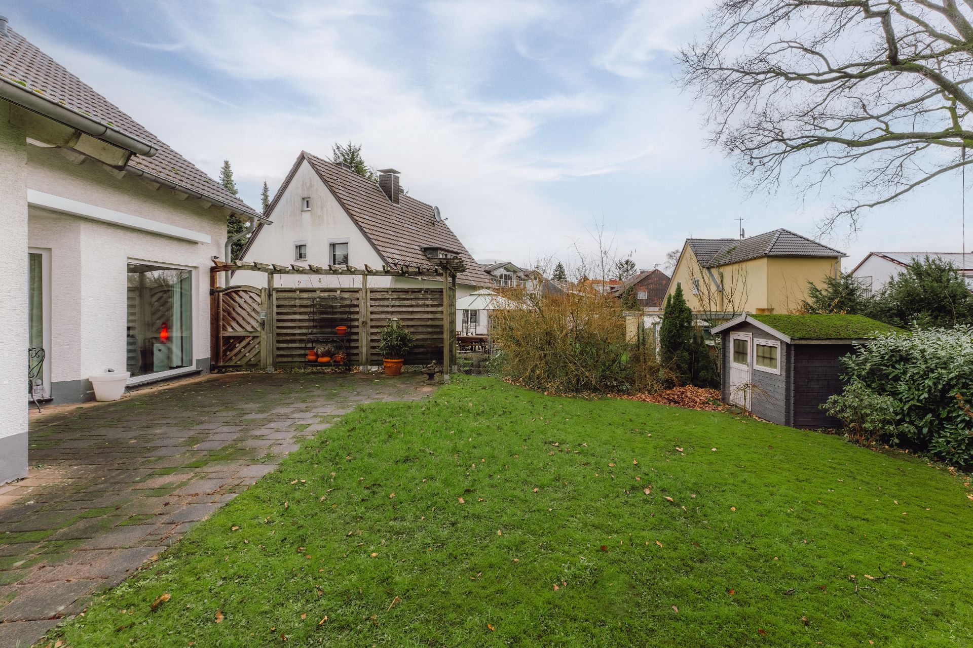 Grüner Garten mit Rasen, kleinem Schuppen und angrenzender Terrasse eines Wohnhauses.