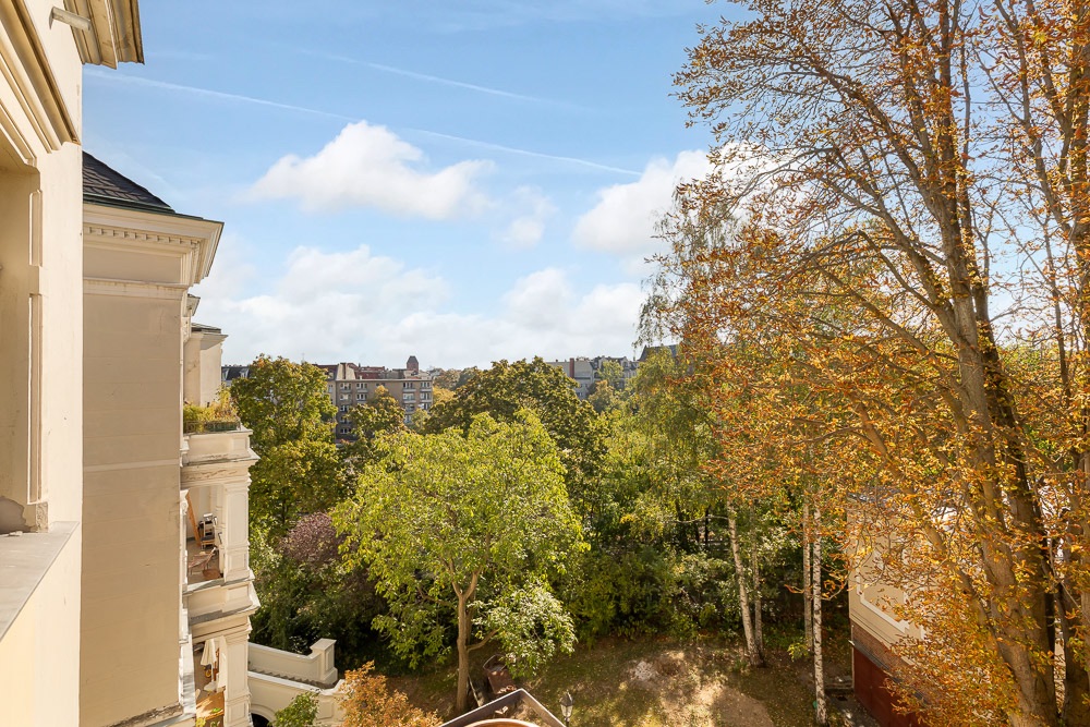 Blick vom Balkon auf einen Garten mit Bäumen und Nachbargebäuden im Hintergrund.