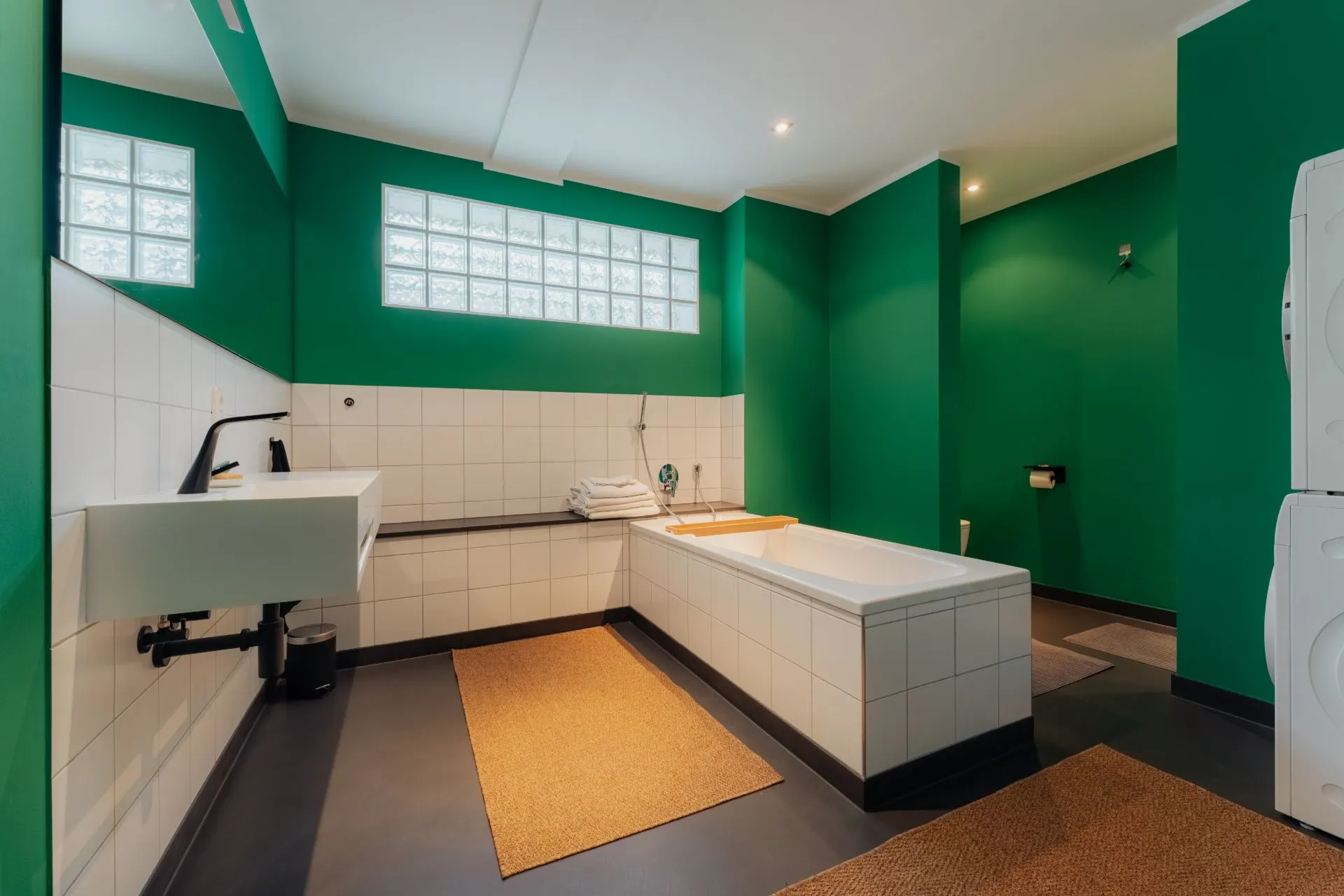 Modernes Badezimmer mit grünen Wänden, Badewanne, Waschbecken und Waschmaschine.