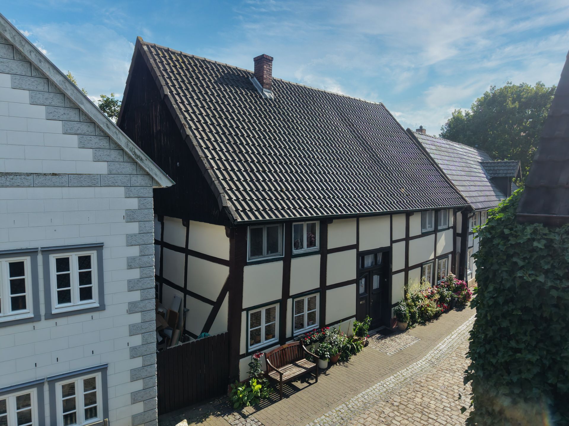 Fachwerkhaus mit Bank und Blumen an einer Kopfsteinpflasterstraße bei Tageslicht.