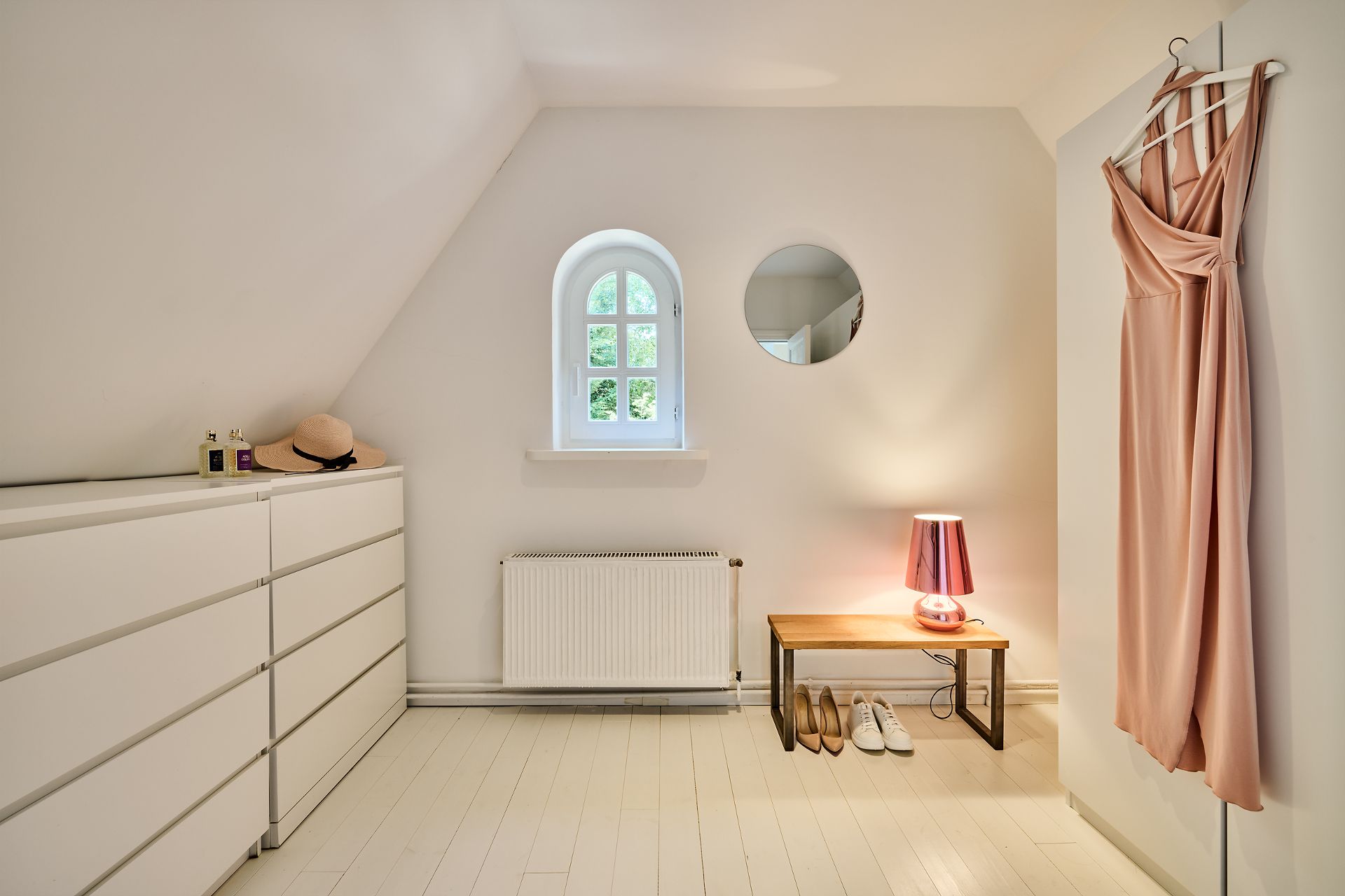 Helles Ankleidezimmer mit Kommode, Bank, Spiegel, Fenster und einem Kleid an der Wand.