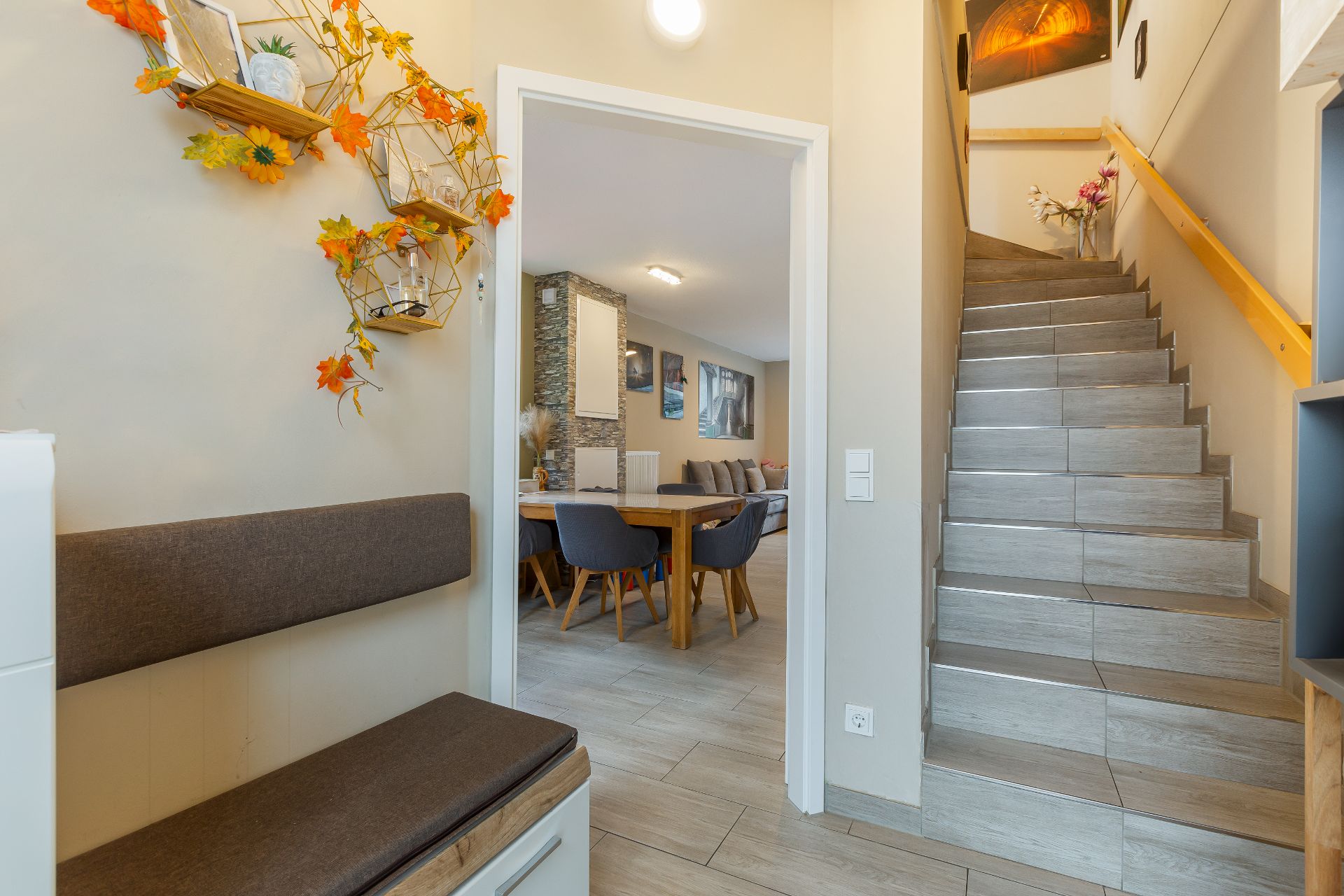 Flur mit Sitzbank, dekorierter Wand und Treppe, Blick ins Wohnzimmer mit Esstisch und Stühlen.