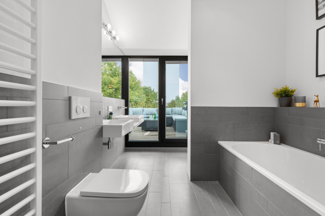 Modernes Badezimmer mit Badewanne, Toilette, Waschbecken und Blick auf Terrasse mit Sitzgruppe.
