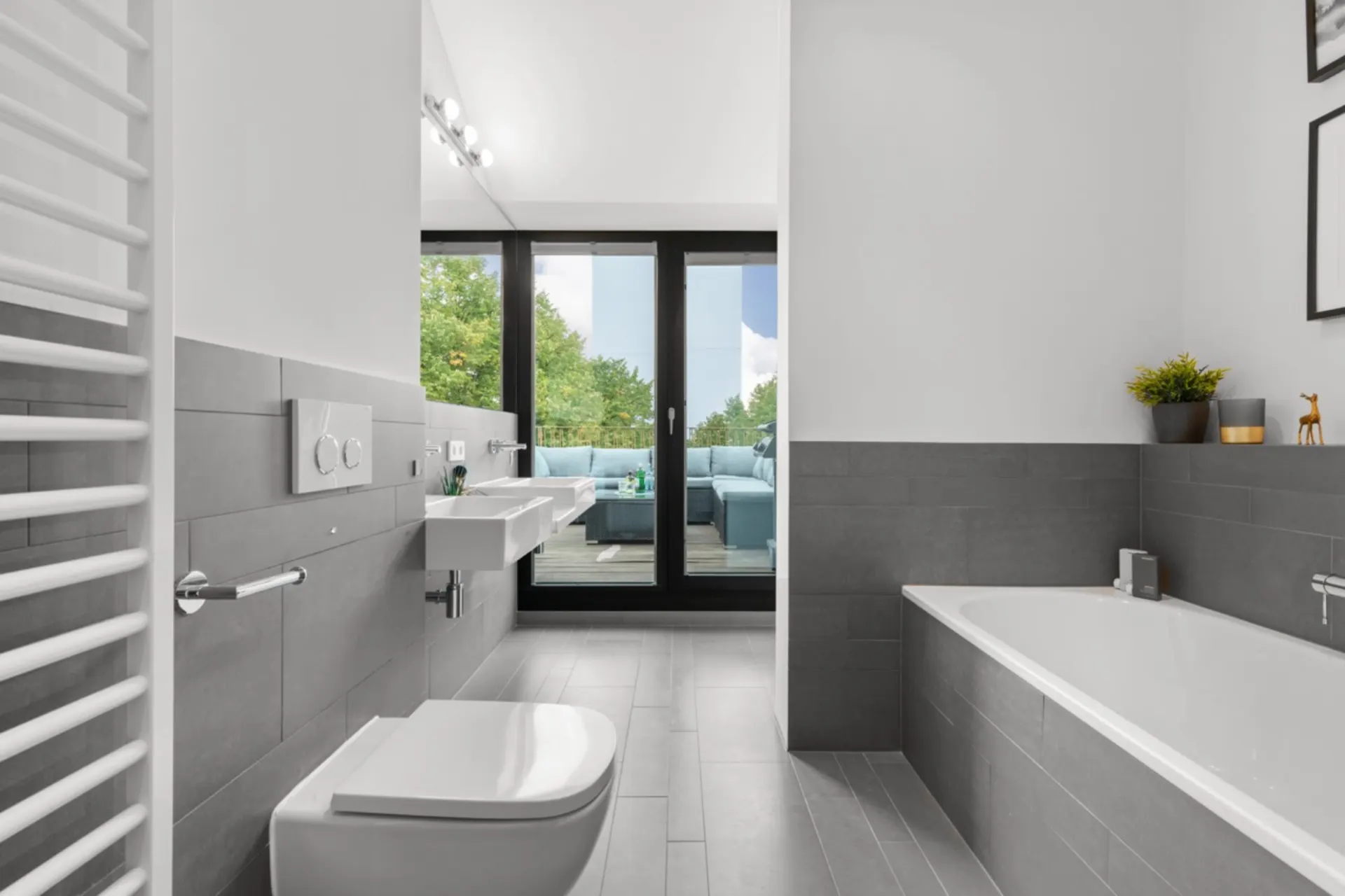 Modernes Badezimmer mit Badewanne, Toilette, Waschbecken und Blick auf Terrasse mit Sitzgruppe.