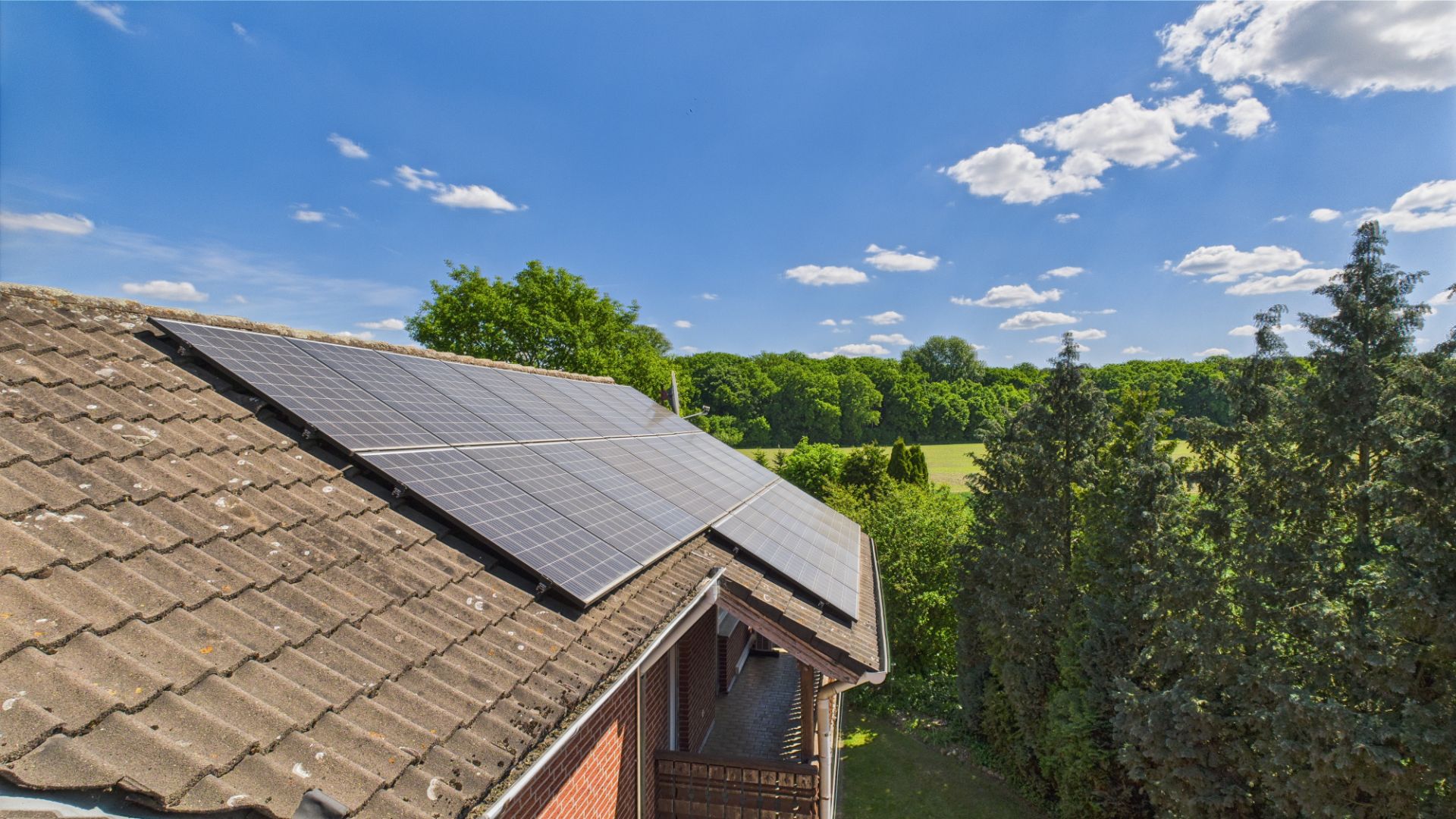 Solaranlage auf dem Hausdach, Bäume und Wiese im Hintergrund bei sonnigem Wetter.