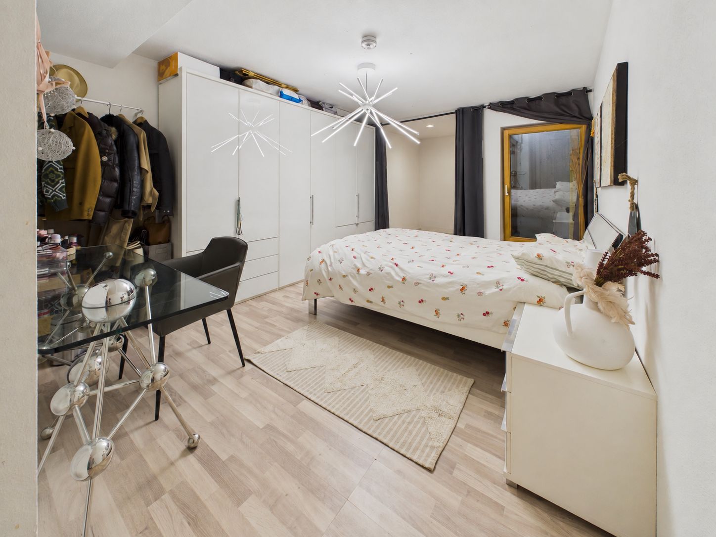 Schlafzimmer mit Doppelbett, Kleiderschrank, Schreibtisch und Stuhl, helle Beleuchtung.
