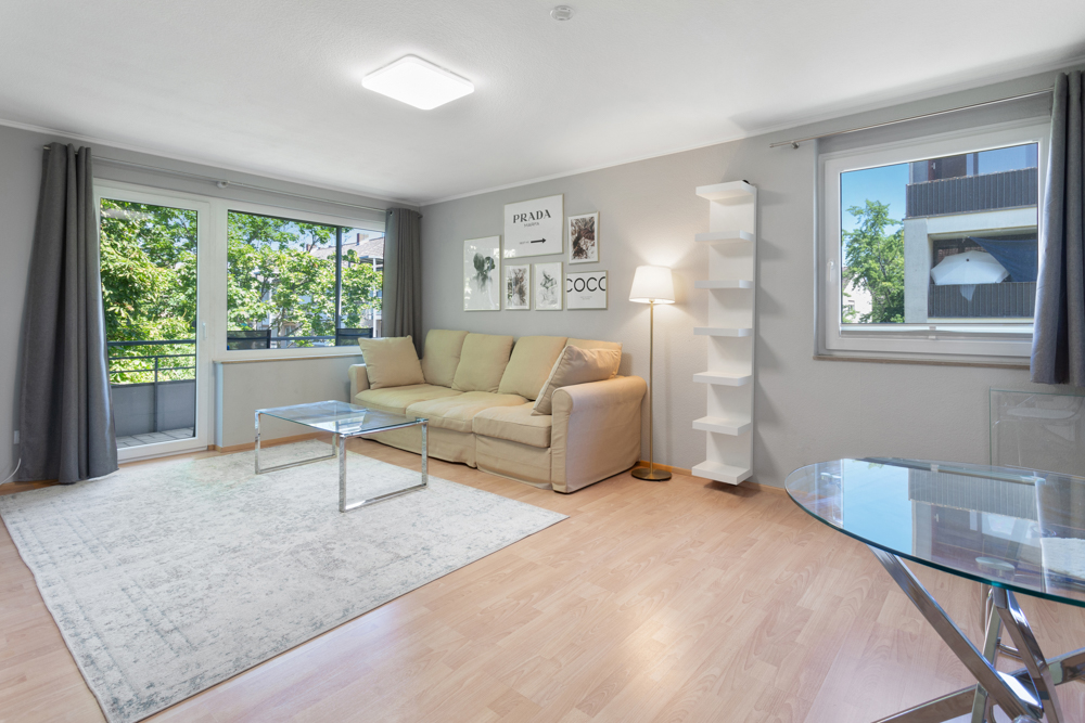 Helles Wohnzimmer mit Sofa, Couchtisch, Teppich und großen Fenstern mit Blick ins Grüne.