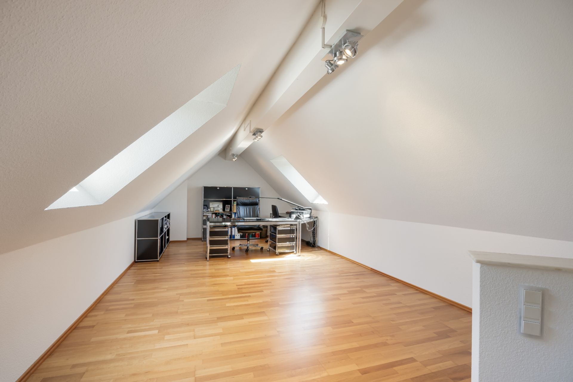 Helles Dachzimmer mit Schreibtisch, Computer und zwei großen Dachfenstern.