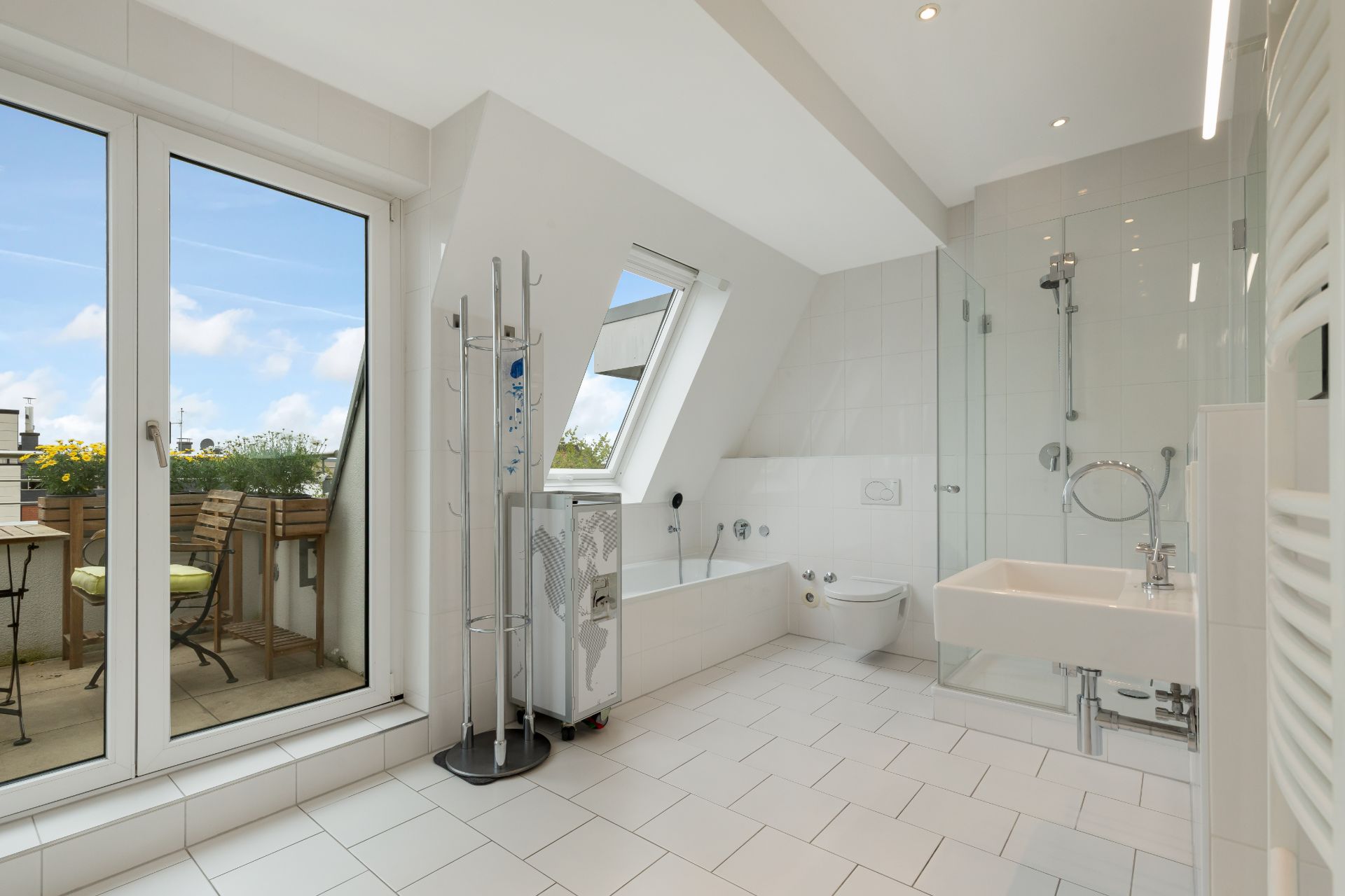 Helles Badezimmer mit Badewanne, Dusche, Waschbecken und Zugang zu einem Balkon mit Sitzgelegenheit.