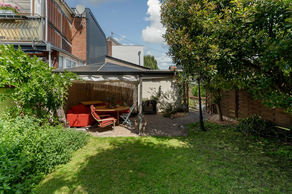 Garten mit überdachter Terrasse, roten Sitzmöbeln und viel Grün.