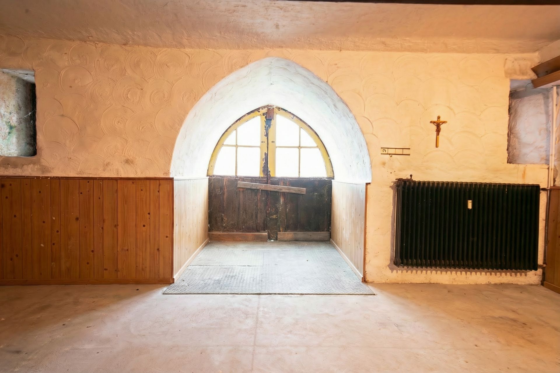 Raum mit gewölbtem Fenster, Holzwand und dunklem Heizkörper an der Wand.