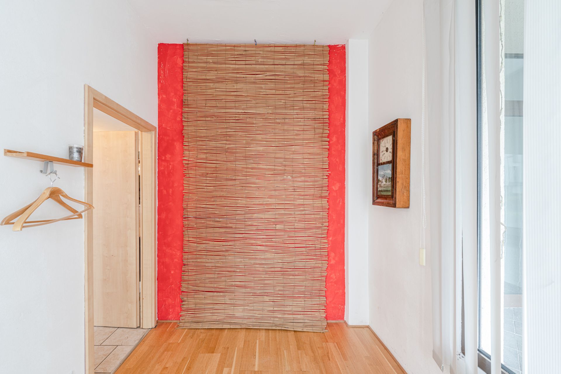 Flur mit Holzfußboden, rotem Wandakzent, Bambusvorhang, Bild und Garderobe mit Kleiderbügeln.